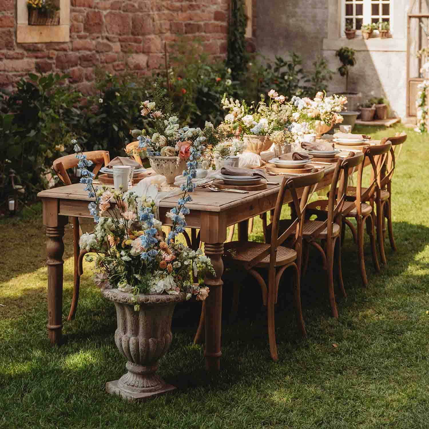 Holztisch im Garten mit Blumenarrangements und gedecktem Geschirr bei Sonnenschein