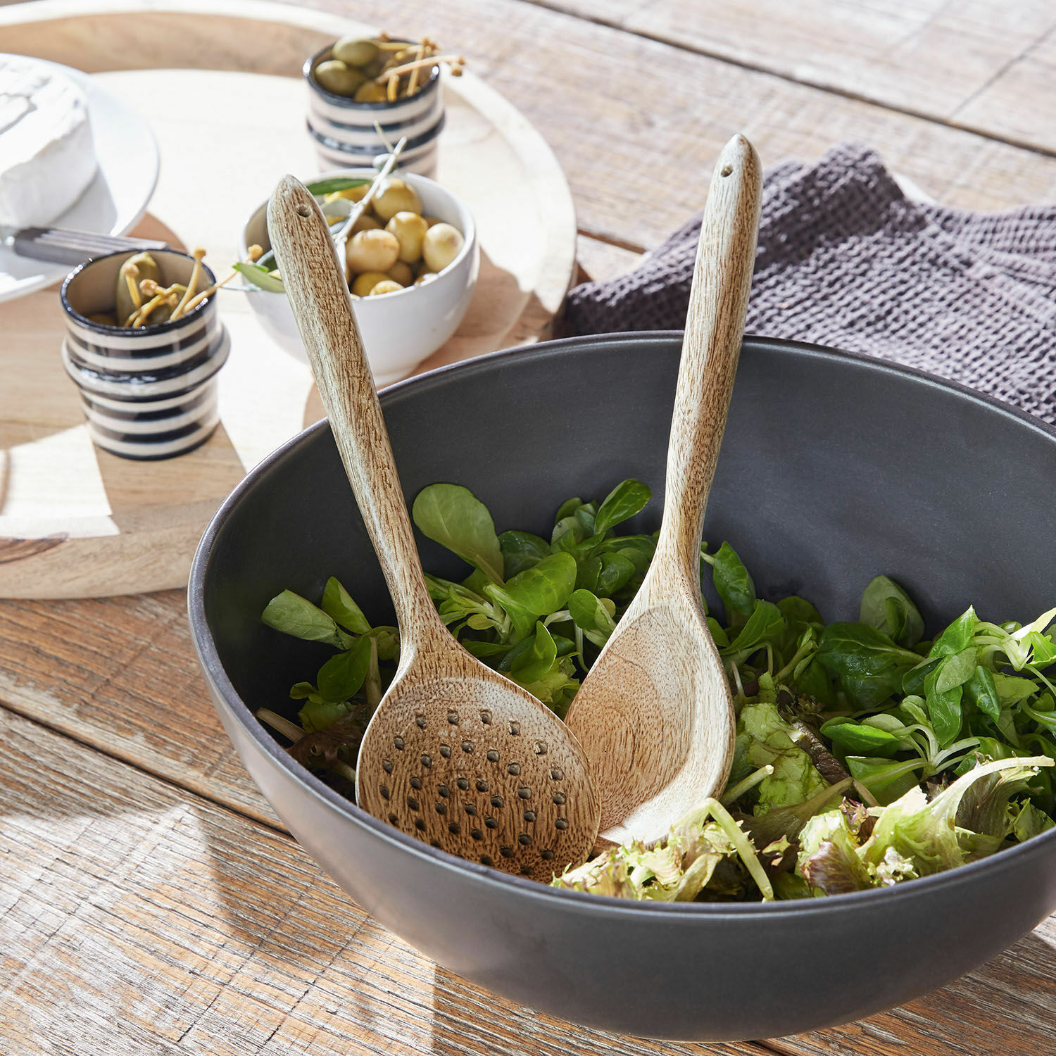 Salatbesteck Helier Schwarze Holzschale mit grünem Salat und Holzsalatbesteck auf rustikalem Holztisch