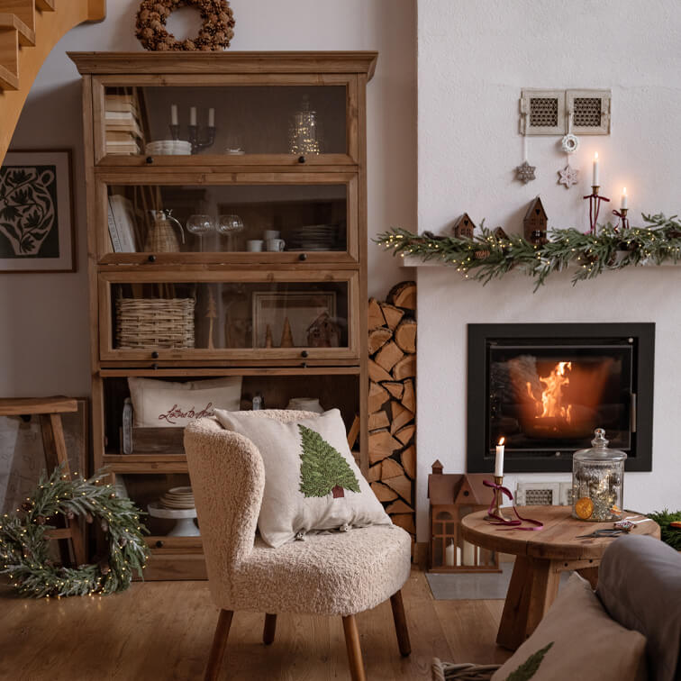 Gemütliches Wohnzimmer mit cremefarbenem Sessel, Holzschrank und weihnachtlich dekoriertem Kamin