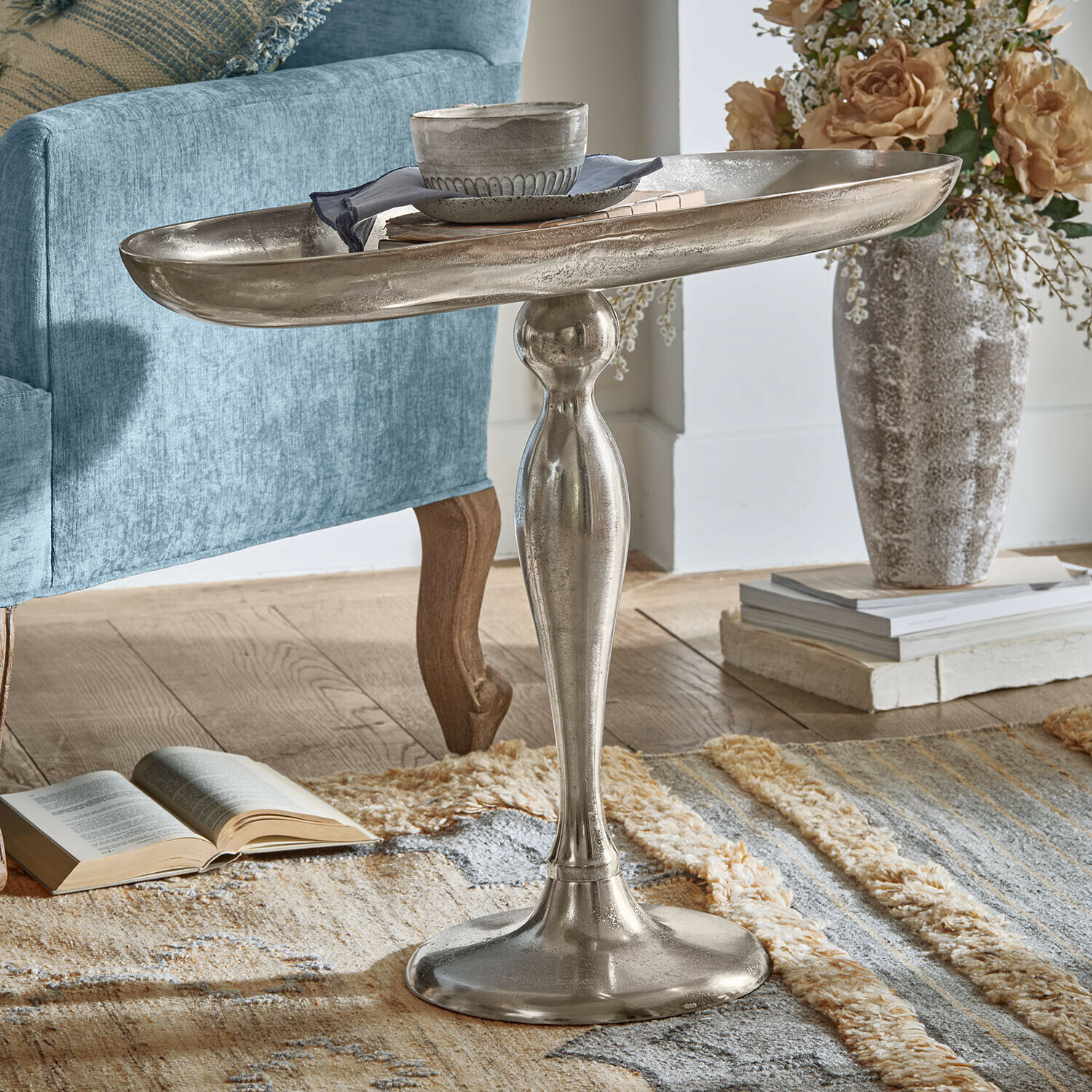 Beistelltisch Stonebrook Silberner Metall-Beistelltisch mit dekorativem Fuss auf Teppich neben blauem Sessel