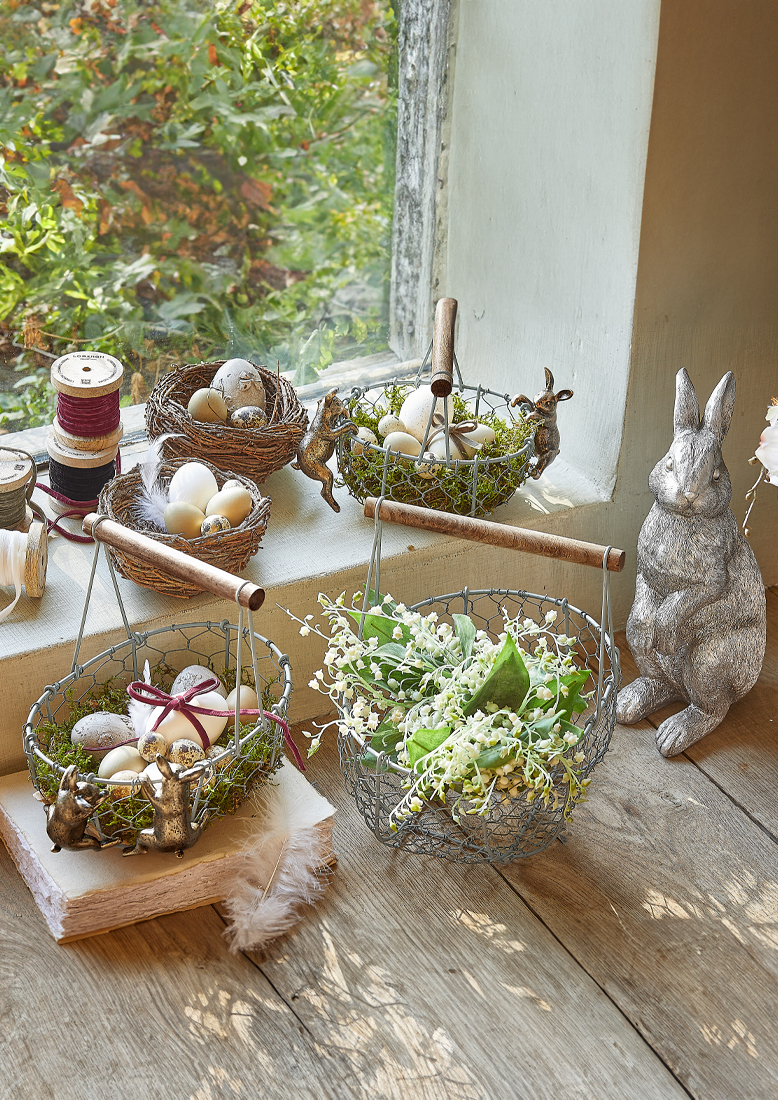 Metallkörbe mit Holzgriffen und Hasendekor, gefüllt mit Eiern und Blumen auf Holzboden