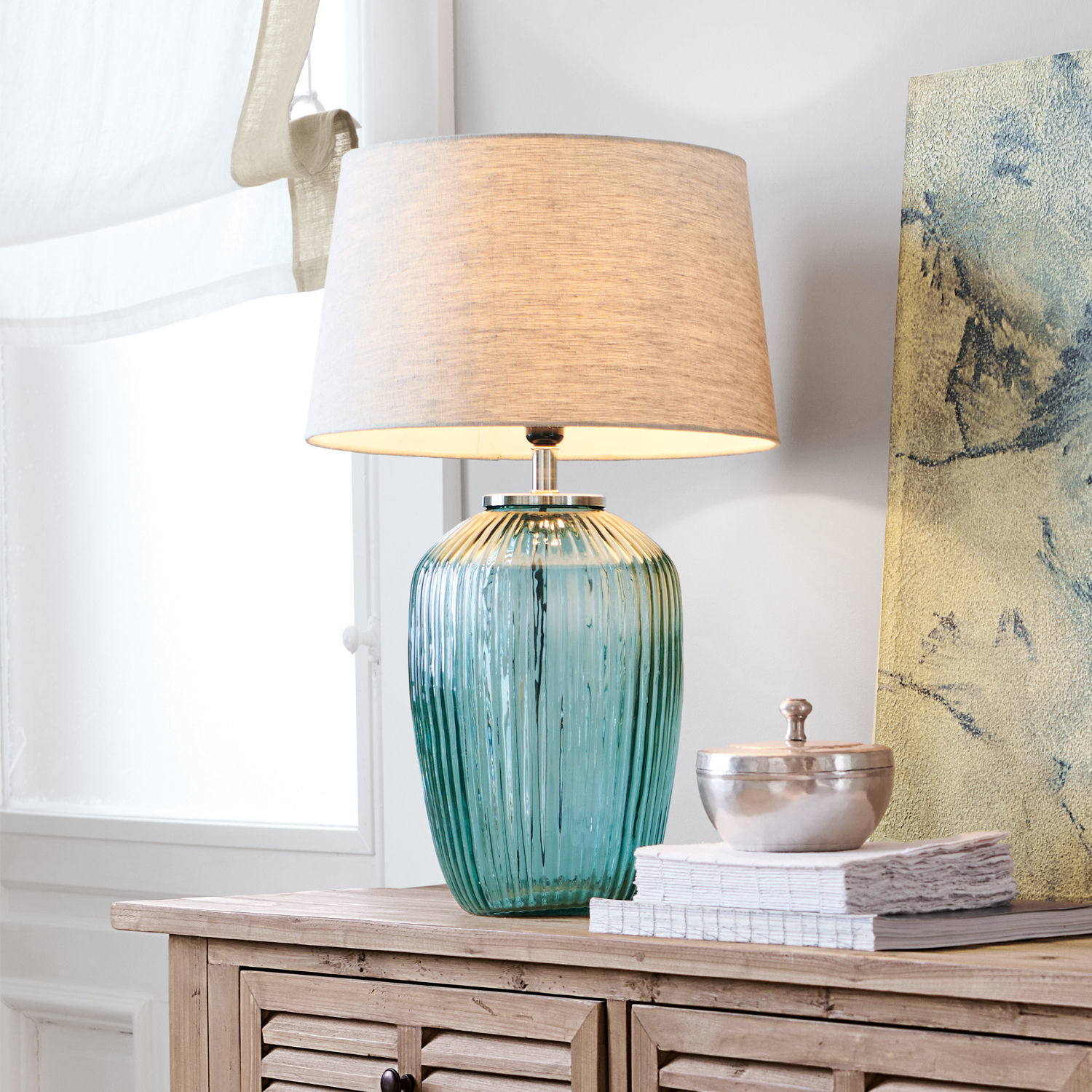 Tischlampe Fenis Tischlampe aus grünem Glas mit beigem Stoffschirm auf heller Holzkommode im Wohnzimmer