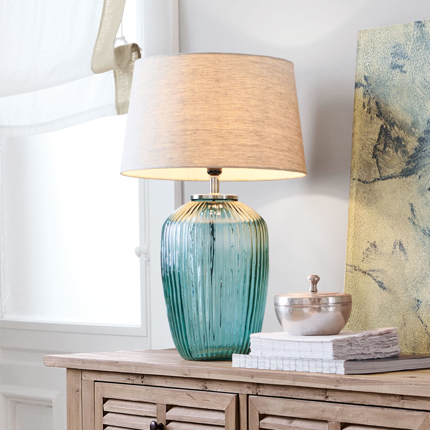 Tischlampe Fenis Tischlampe aus grünem Glas mit beigem Stoffschirm auf heller Holzkommode im Wohnzimmer