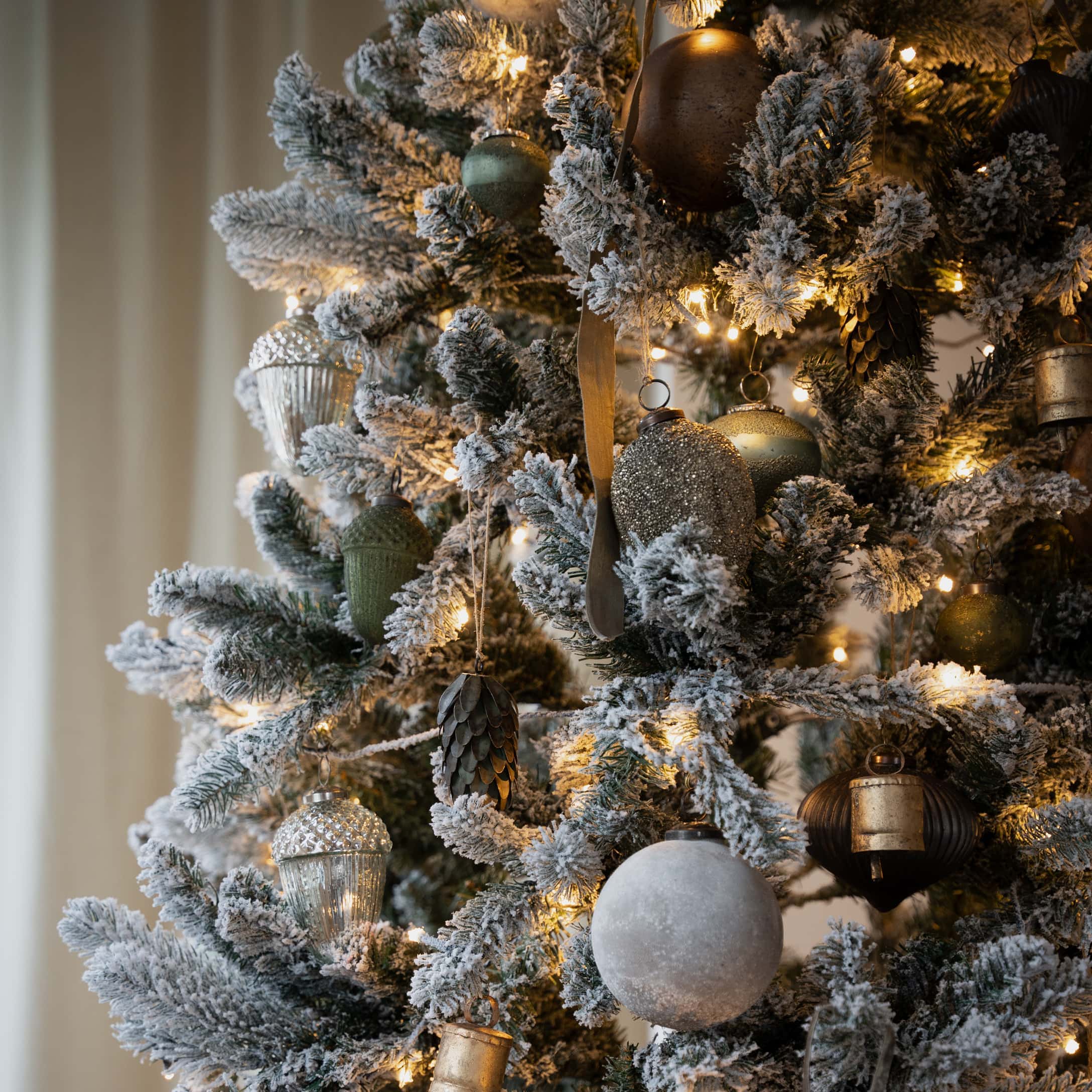 Künstlicher Weihnachtsbaum mit schneebedeckten Zweigen und goldgrünem Christbaumschmuck, festliche Dekoration