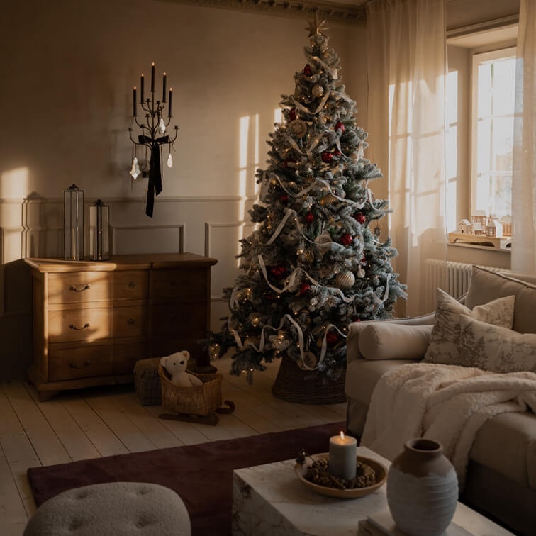 Gemütliches Wohnzimmer mit geschmücktem Weihnachtsbaum, Holzkommode und brennendem Wandkerzenhalter