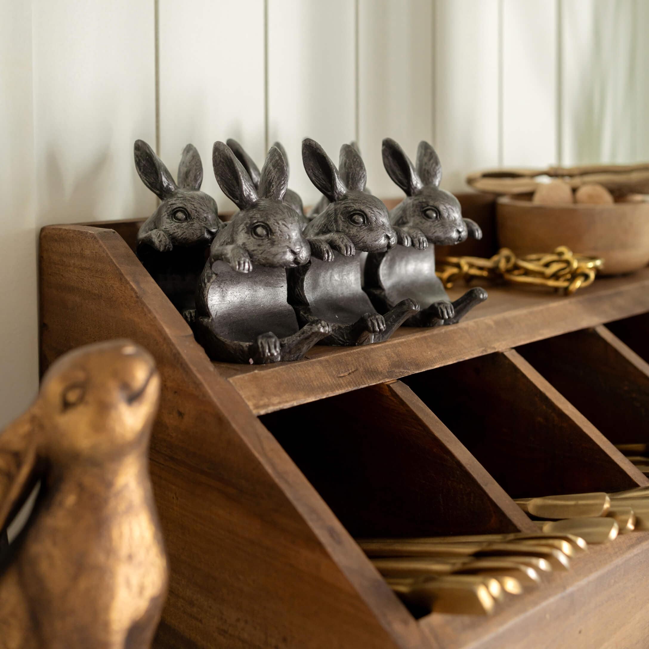 Vier dunkelgraue Metall-Hasenfiguren auf einem Holzregal mit Fächern zur Dekoration