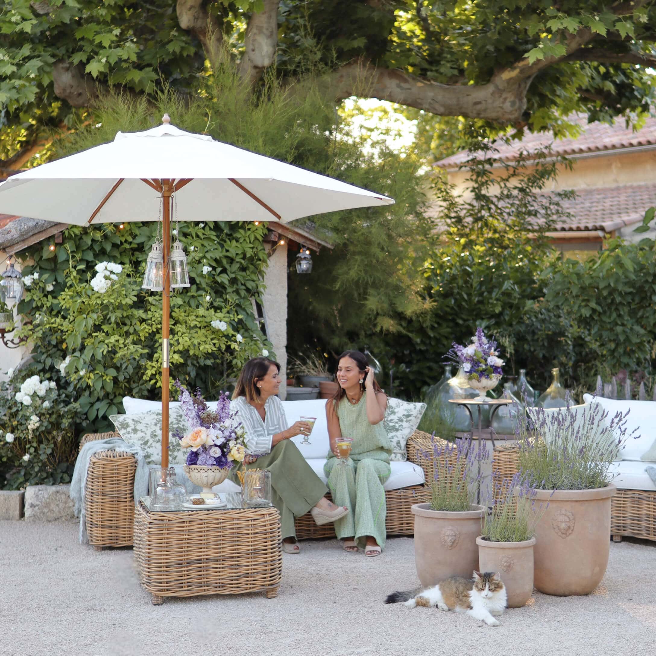 Gartenmöbel aus natürlichem Rattan mit weissen Kissen und Sonnenschirm, dekoriert mit Lavendeltöpfen
