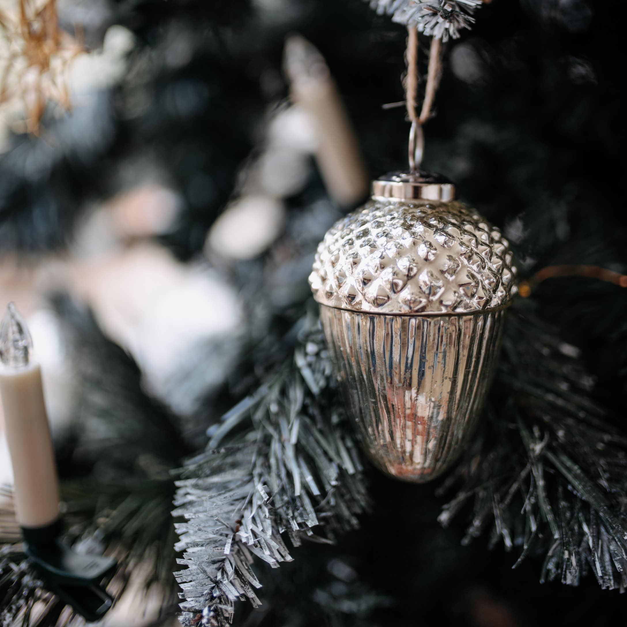 Silberner Weihnachtsbaumschmuck in Eichelform mit Struktur, an grünem Tannenzweig hängend