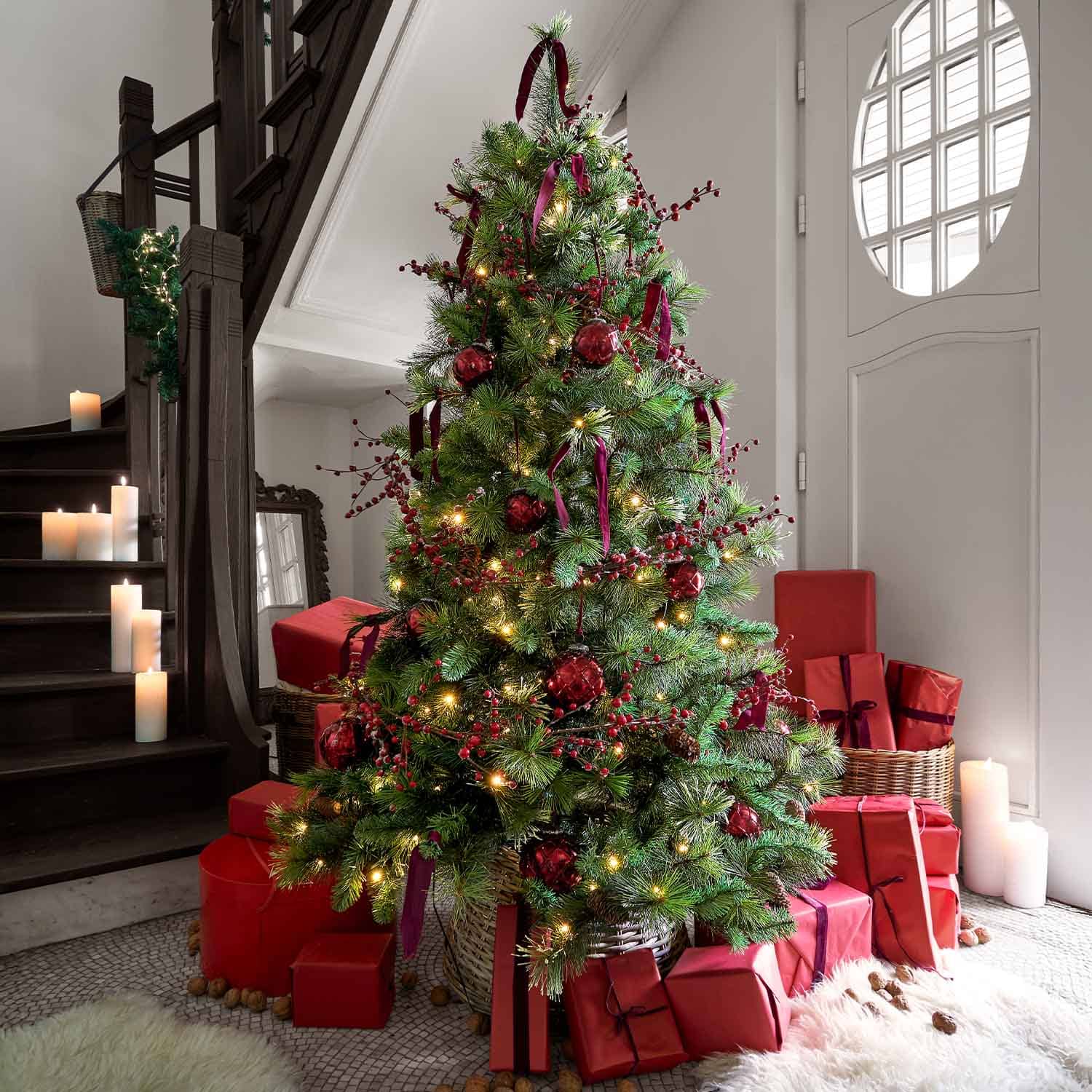 Weihnachtsbaum mit grünen Zweigen, roten Kugeln und roten Geschenkpaketen darunter im Wohnzimmer