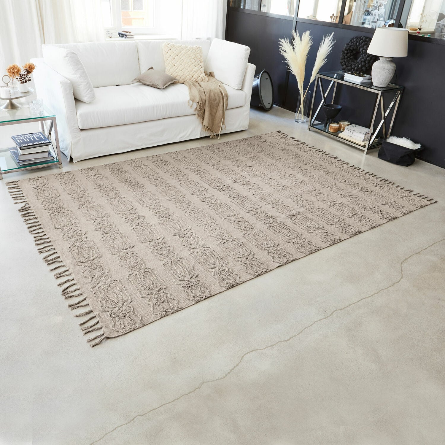 Beiger Baumwollteppich mit Fransen und Muster in modernem Wohnzimmer mit weissem Sofa und Dekorationen