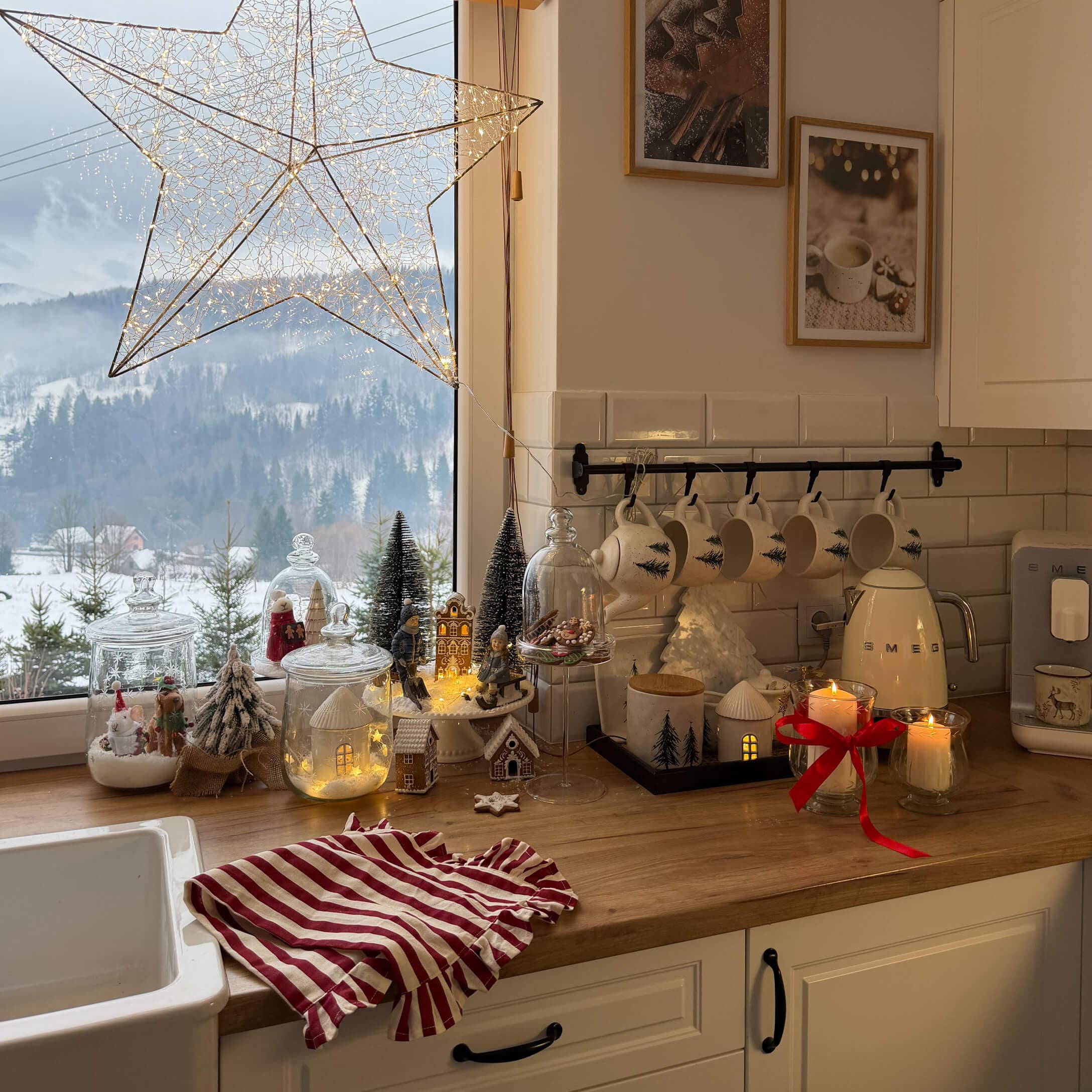 Küche mit Holzarbeitsfläche und Weihnachtsdekoration, weisse Tassen mit Tannenbaum-Motiv und LED-Lichterkette