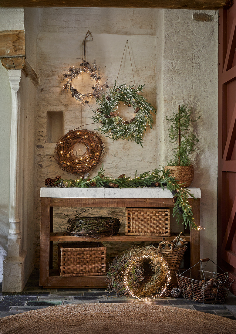 Weihnachtliche Dekokränze aus Zweigen und Lichterketten an Wand und Holztisch mit Marmorplatte