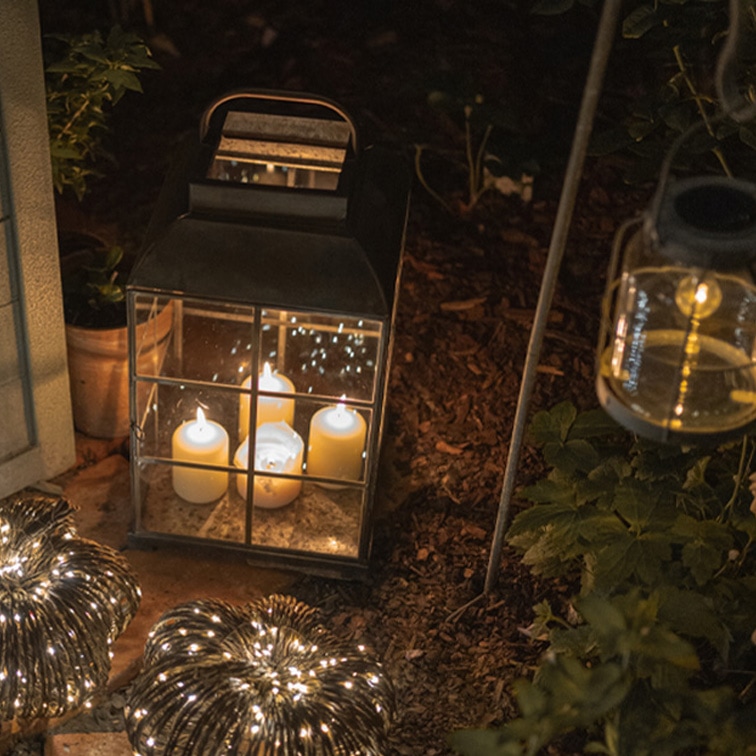 Metalllaterne mit vier weissen Kerzen und dekorativen Lampions im Garten bei Nacht