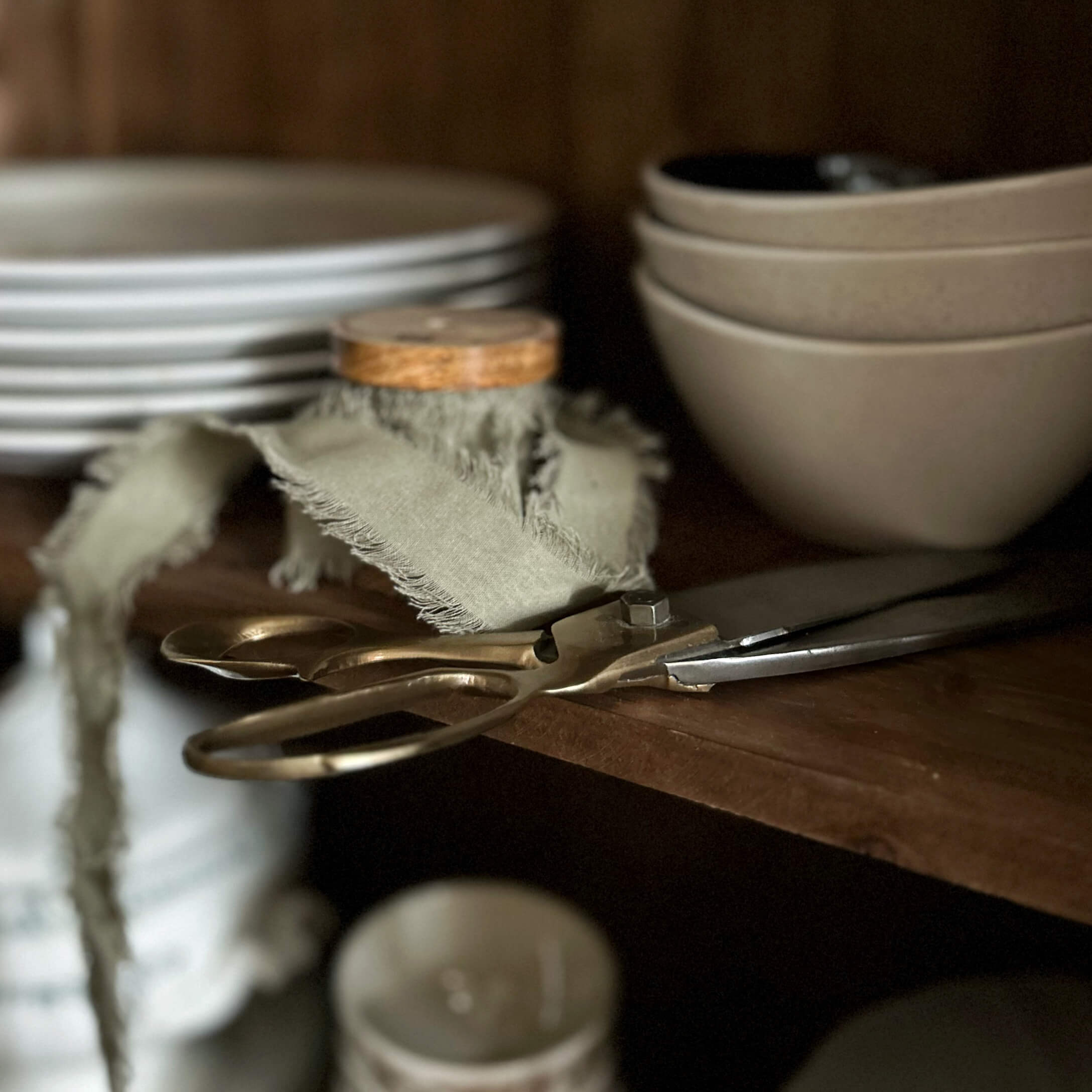 Alte Messing-Schere auf Holzregal neben beigen Schalen und Tellern in der Küche