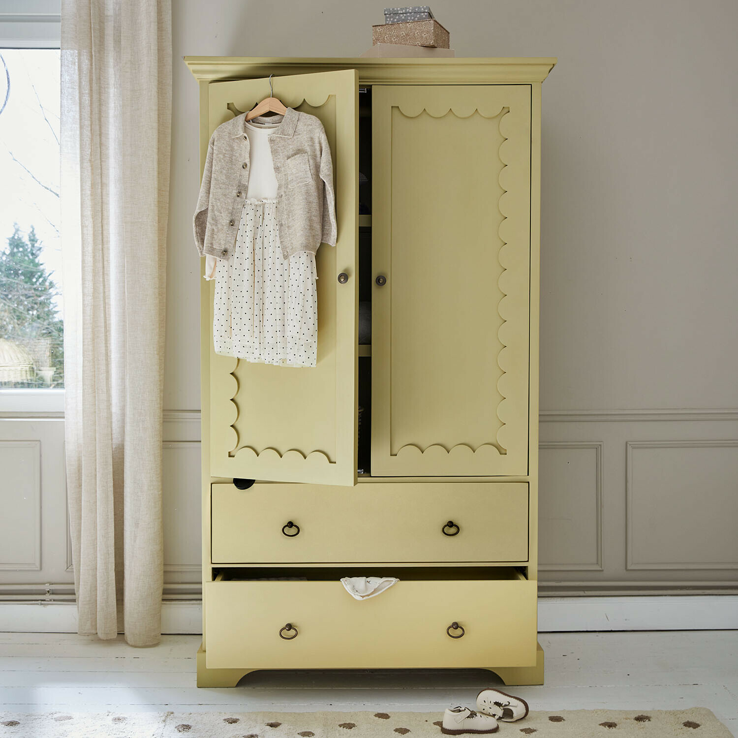 Kinderkleiderschrank Frollin Gelber Holzschrank mit dekorativen Türen und Kinderkleidung an der Tür in hellem Raum