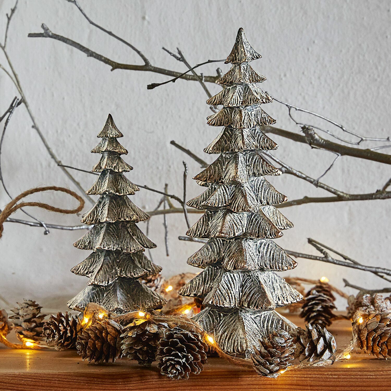 Deko-Baum 2er Set Calavi Dekorative silberne Metall-Weihnachtsbäume auf Holztisch mit Lichterkette und Tannenzapfen.