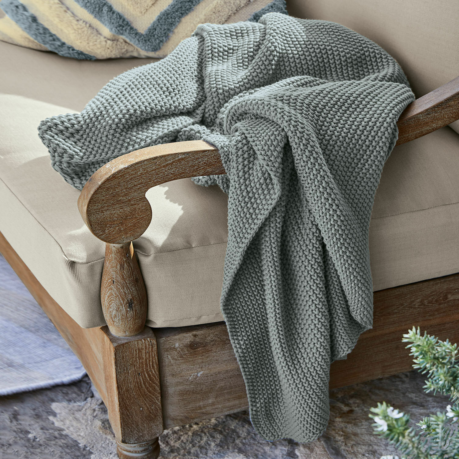 Plaid Ancy Grau gestrickte, dicke Decke aus weicher Wolle auf einem Holzstuhl mit beigem Polster.
