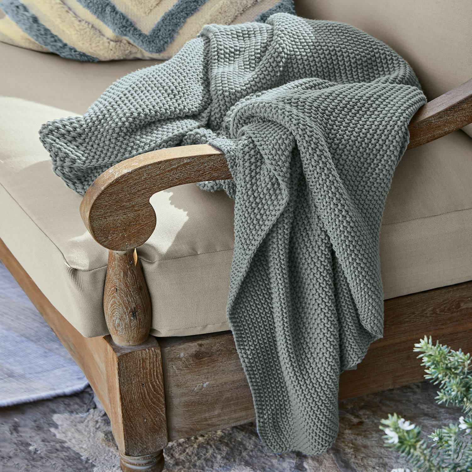 Plaid Ancy Grau gestrickte, dicke Decke aus weicher Wolle auf einem Holzstuhl mit beigem Polster.