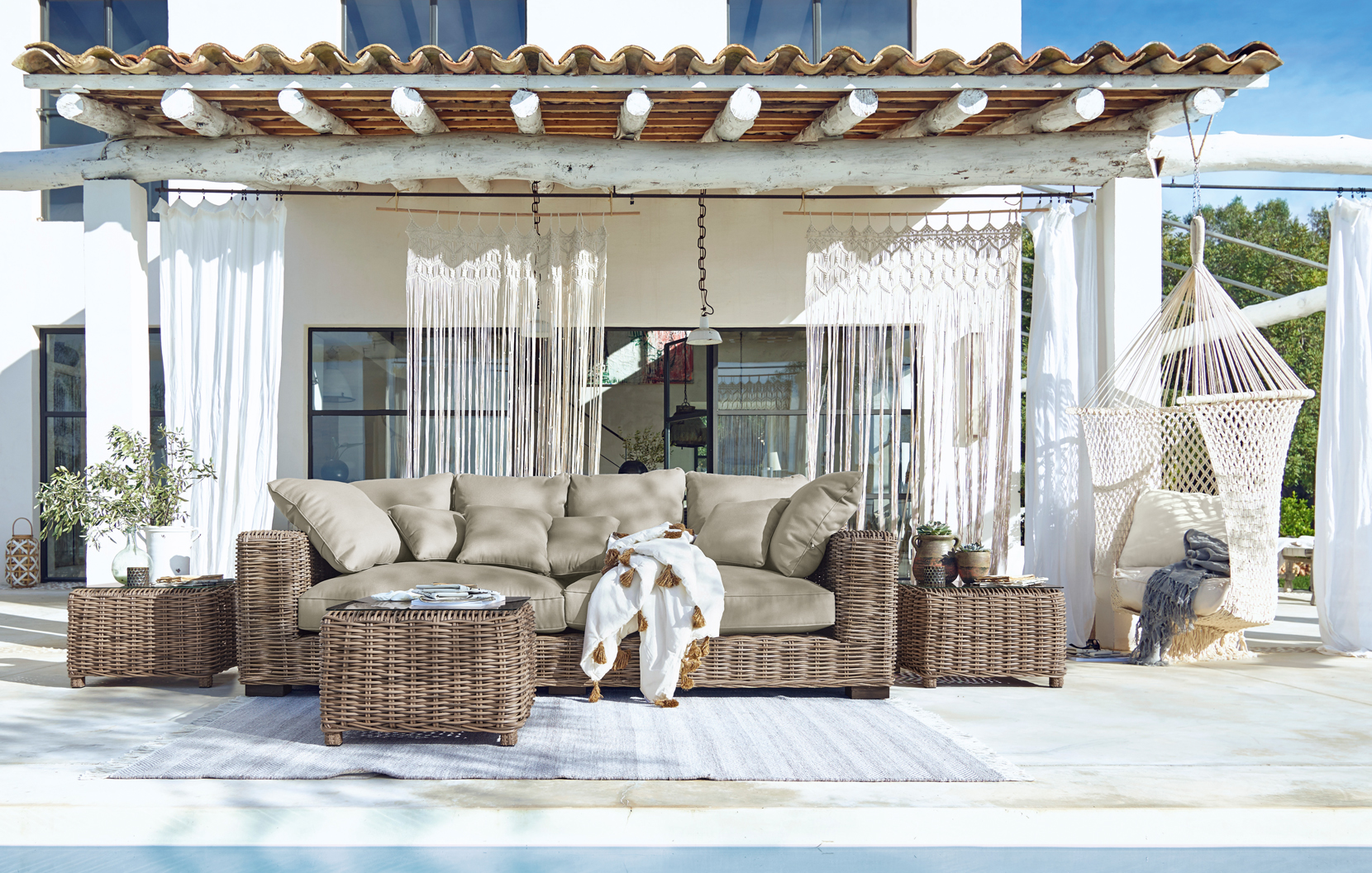 Gartenmöbel-Set aus Rattan mit beigen Polstern auf Terrasse mit Hängesessel und Boho-Dekor.