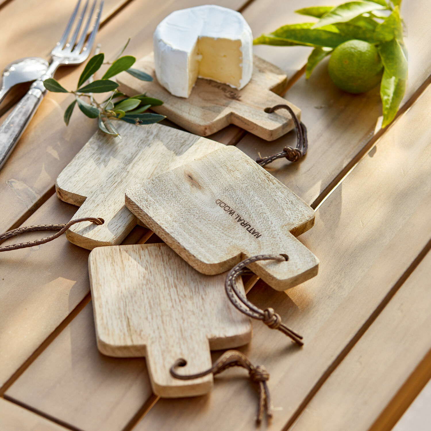 Schneidebrett 4er Set Boise Set aus natürlichen Holz-Schneidebrettern mit Griffen und Schnüren auf Tisch mit Käse und Limette