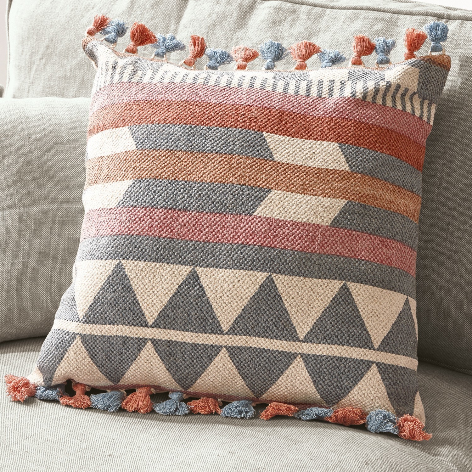 Kissen Mally Dekoratives Baumwollkissen mit geometrischem Muster und blauen sowie orangen Quasten auf hellem Sofa