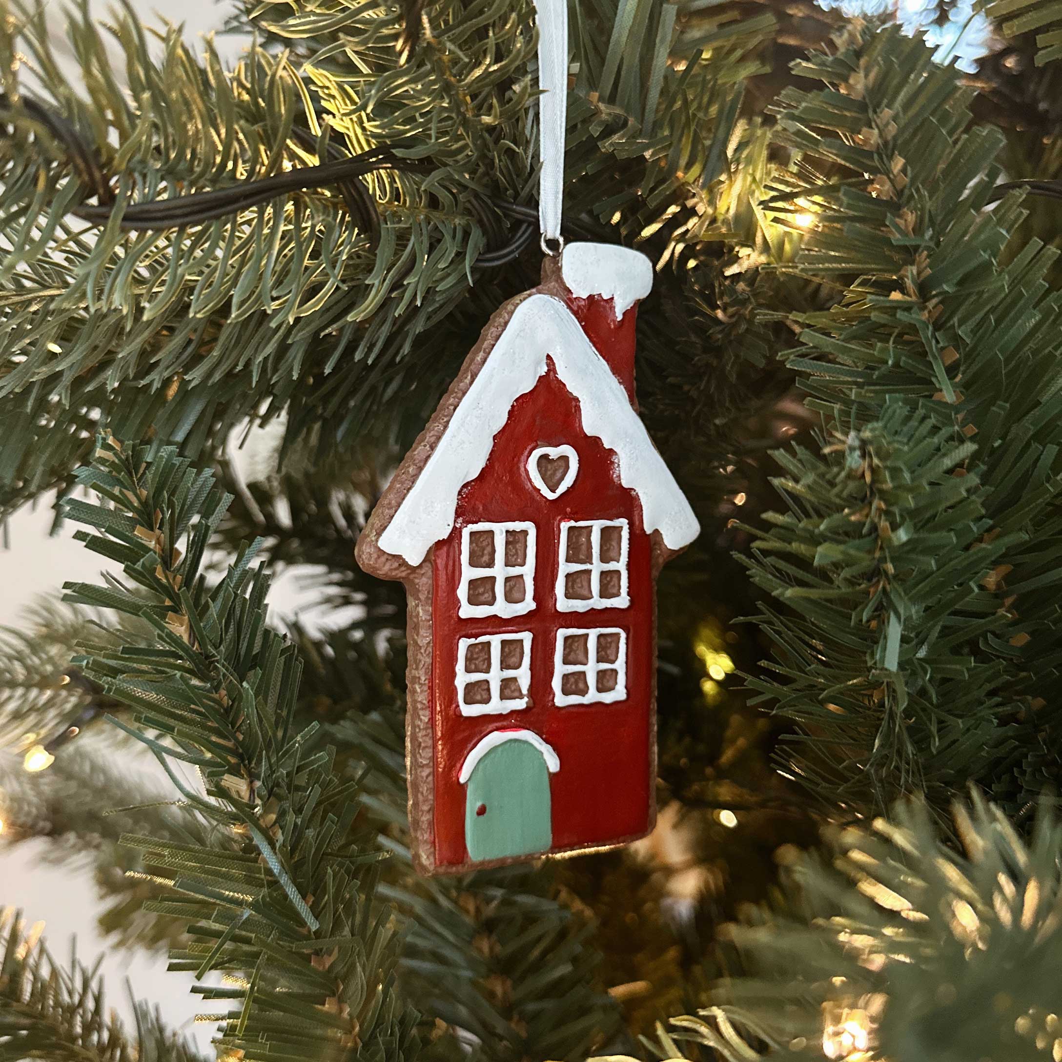 Rotes Keramik-Weihnachtshaus mit weissem Dach und grüner Tür als Baumschmuck am Tannenbaum