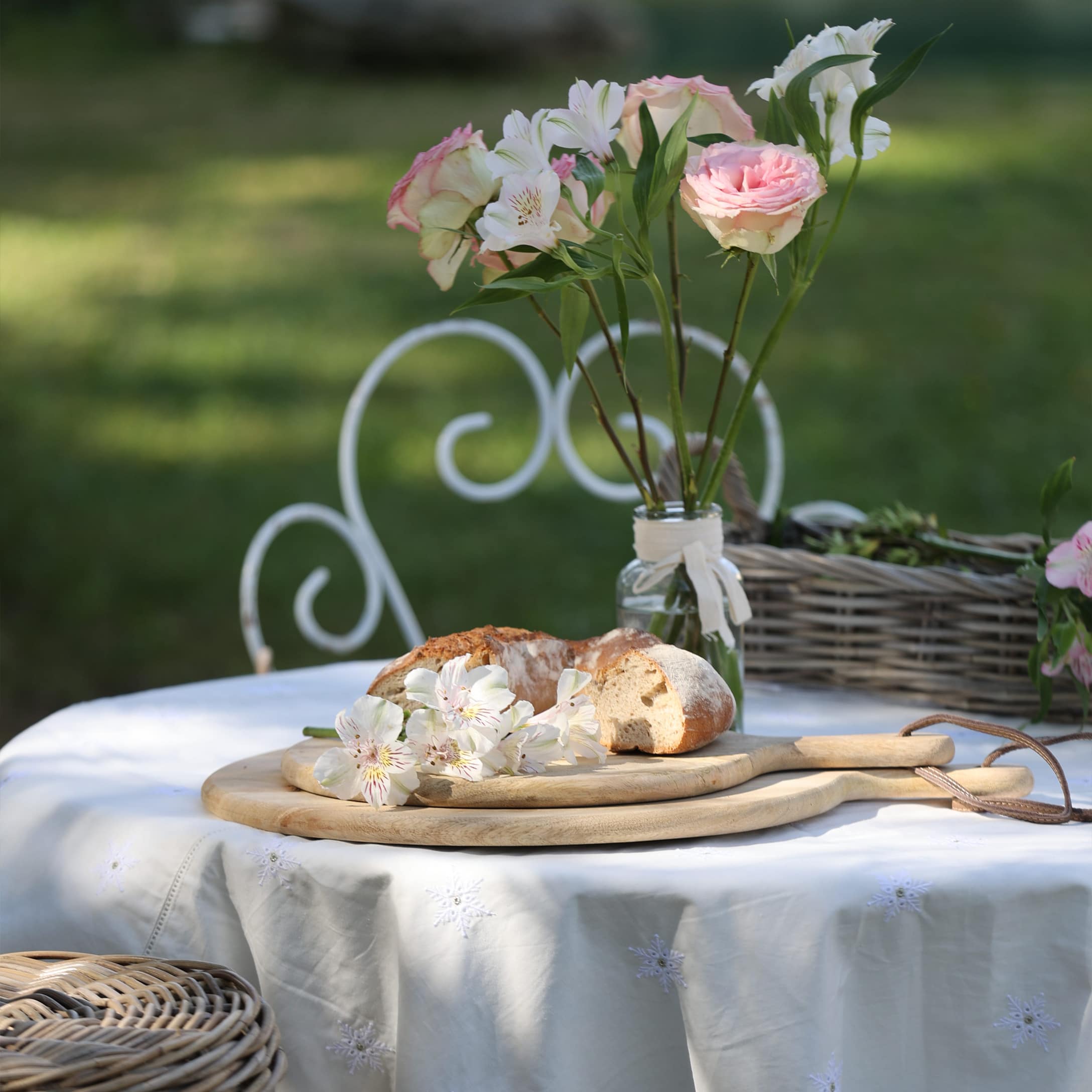 Holz-Schneidebretter mit Brot und Blumen auf weisser Tischdecke im Garten