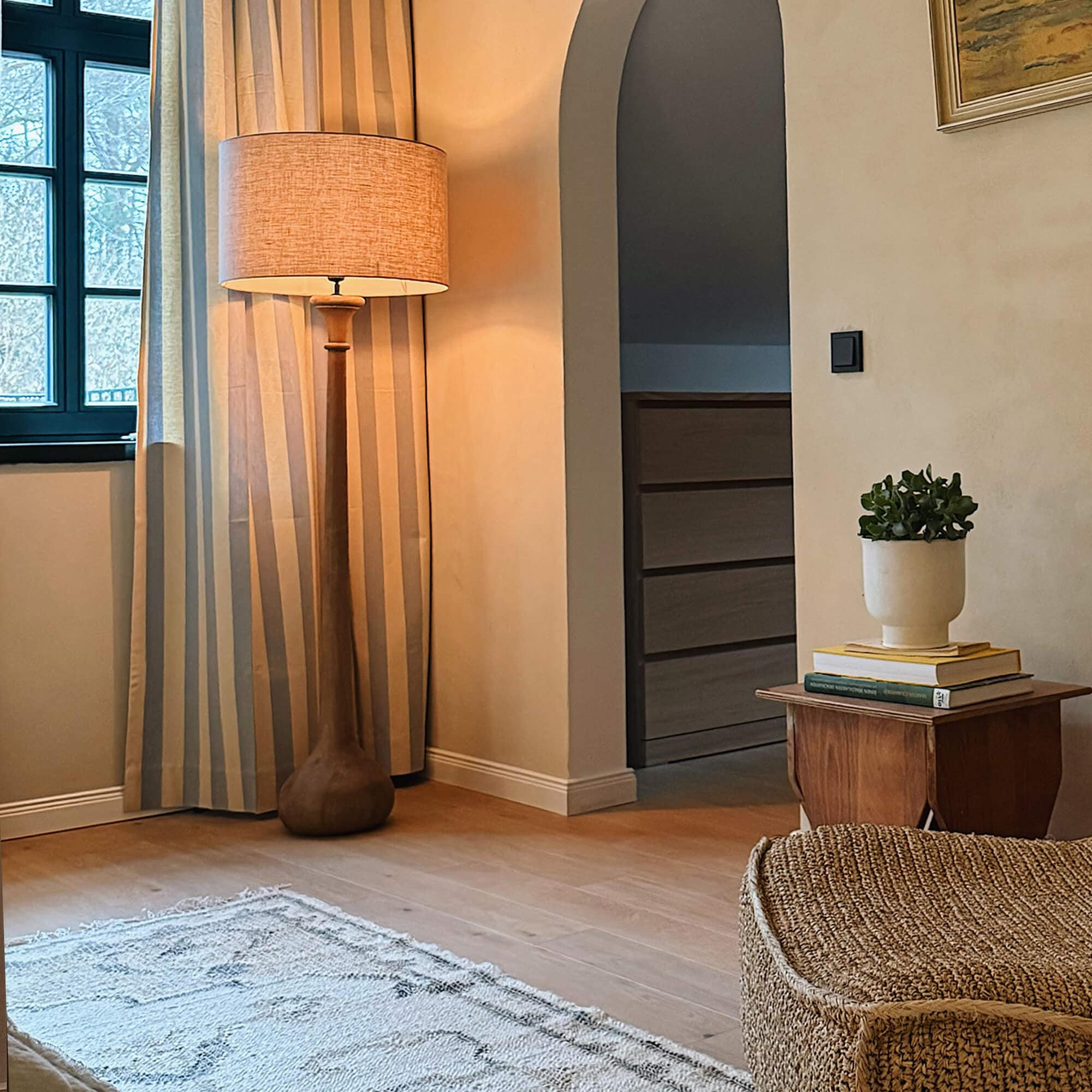 Stehlampe mit Holzfuss und beigem Lampenschirm in gemütlichem Wohnzimmer mit Teppich