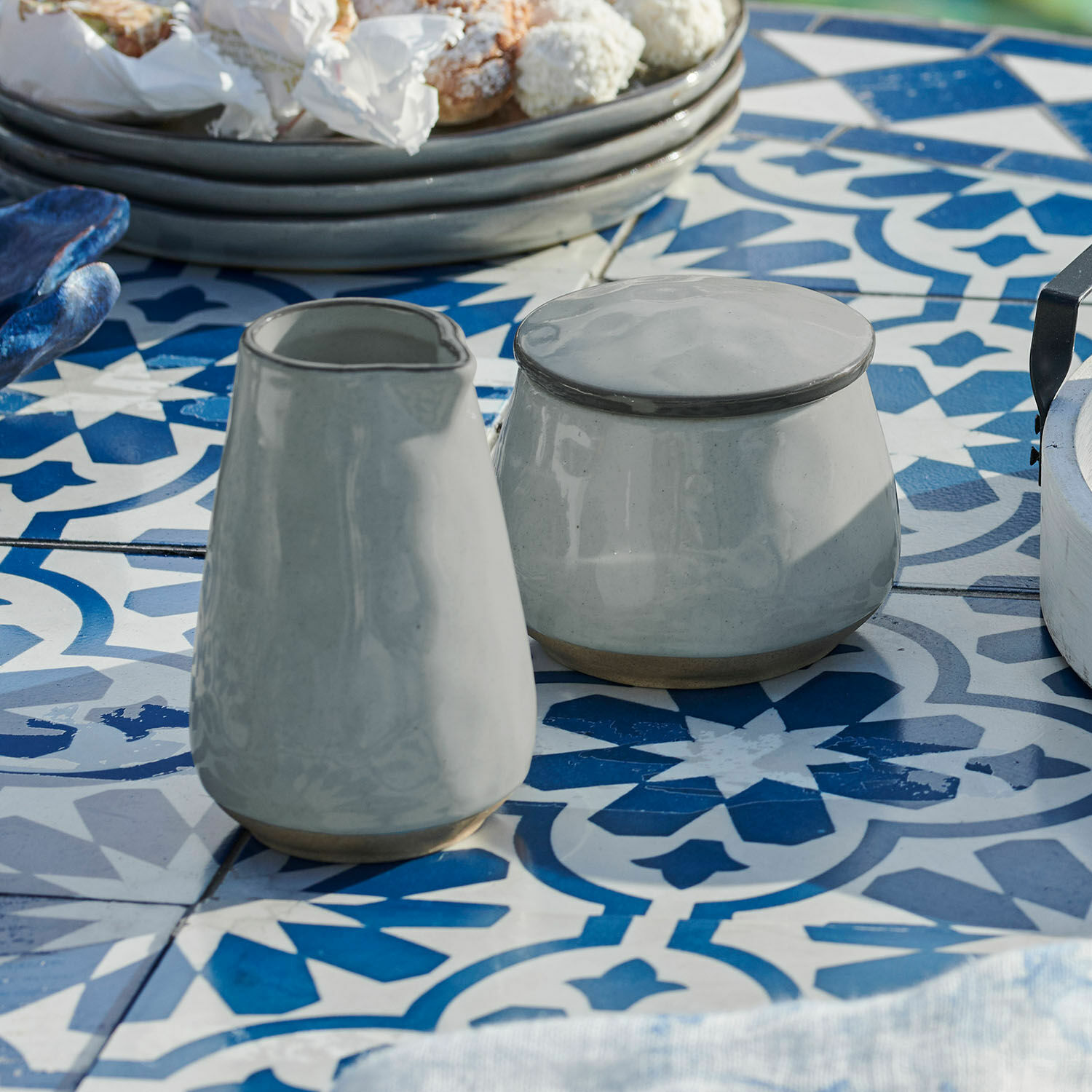 Graue Keramik-Zuckerdose und Milchkännchen auf blau-weiss gemustertem Esstisch