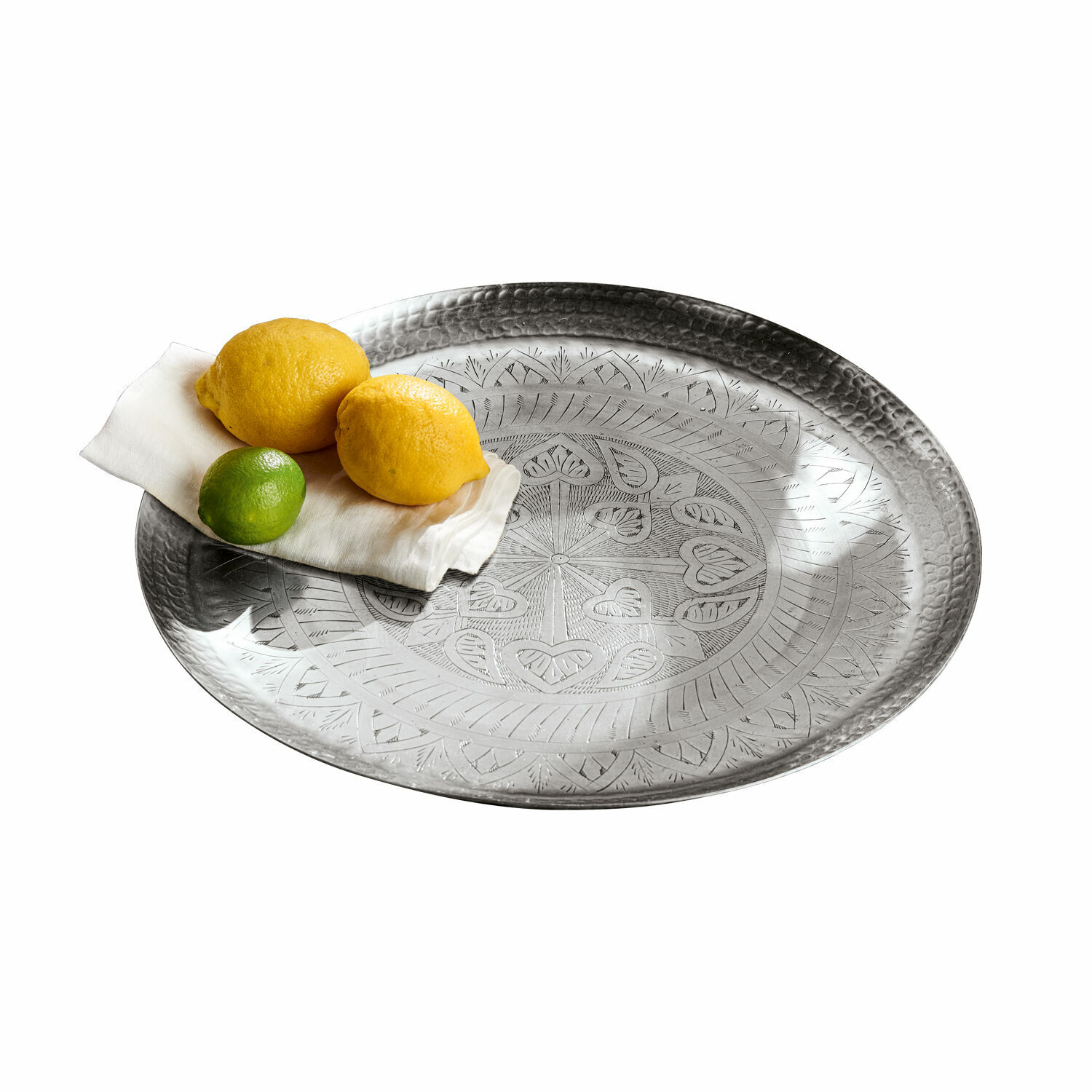 Rundes Metalltablett mit graviertem Muster in Silber, darauf Zitronen und Limette auf weisser Serviette
