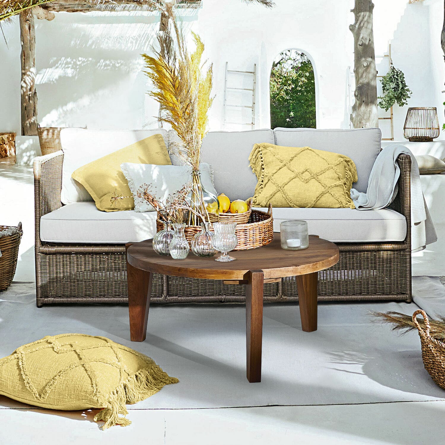 Sofa Lesmont Wohnbereich mit Rattansofa, hellgrauen Kissen und rundem Holzcouchtisch auf sonniger Terrasse