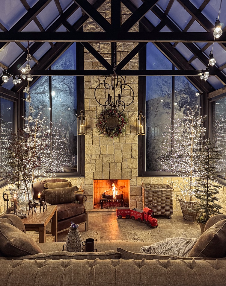 Gemütliches Wohnzimmer mit Cheminée, Weihnachtsdekoration und beleuchteten Bäumen in der Orangerie.