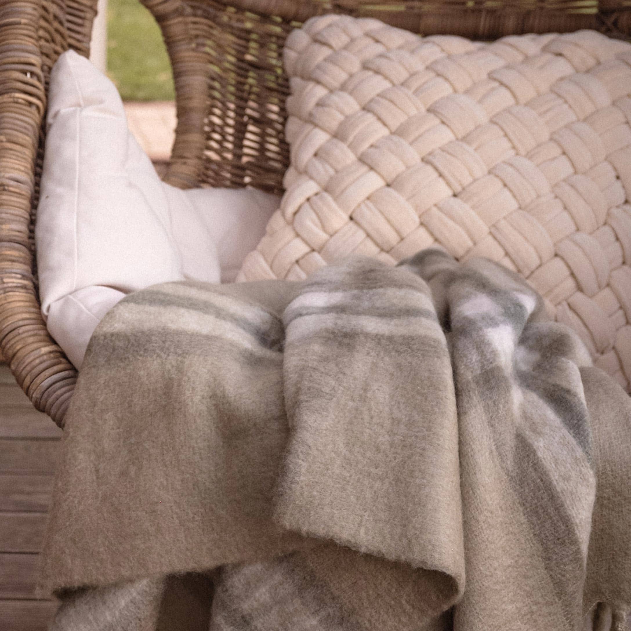Beiger, weicher Plaid mit dezentem Muster auf Rattansessel mit Kissen auf der Terrasse