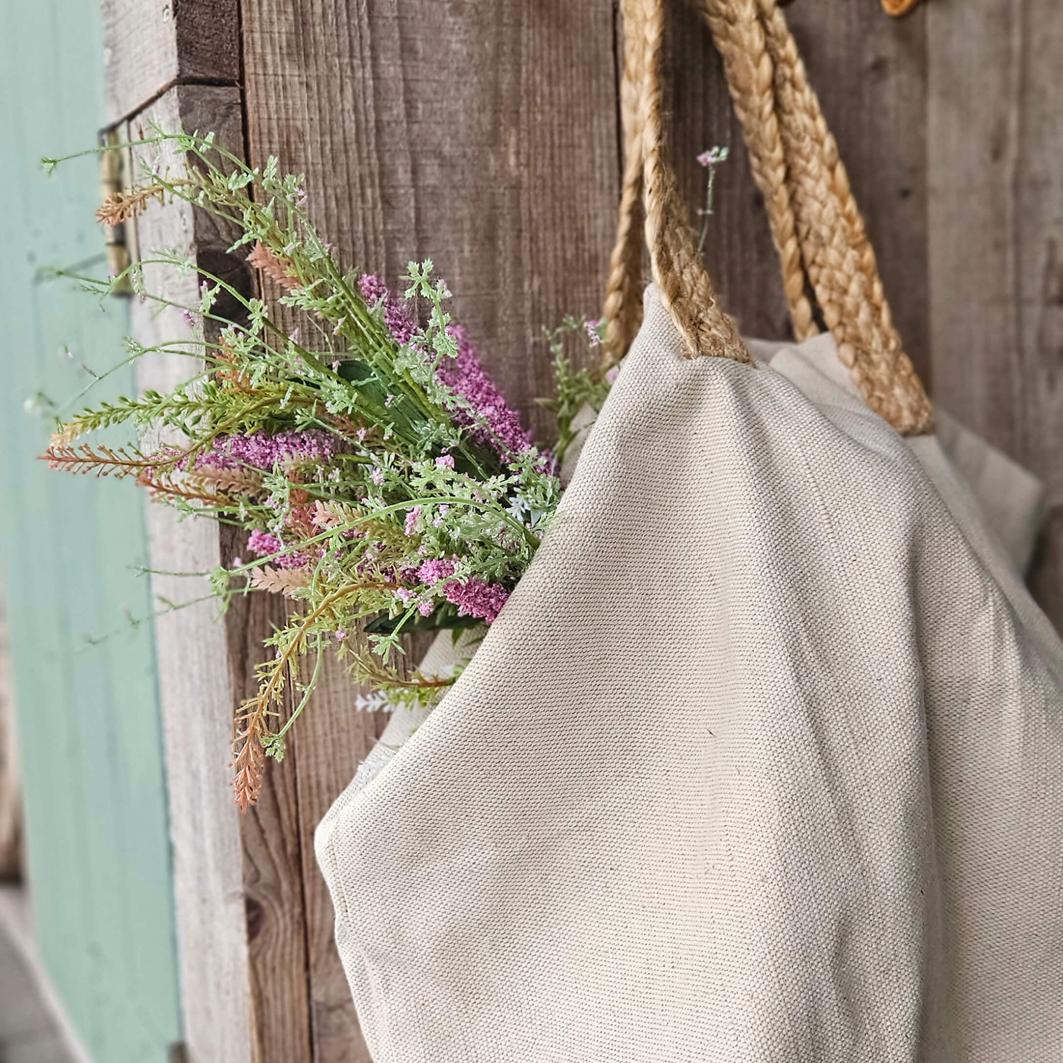 Beigetöne Tasche aus Naturmaterial mit geflochtenen Griffen und Blumen vor rustikalem Holz