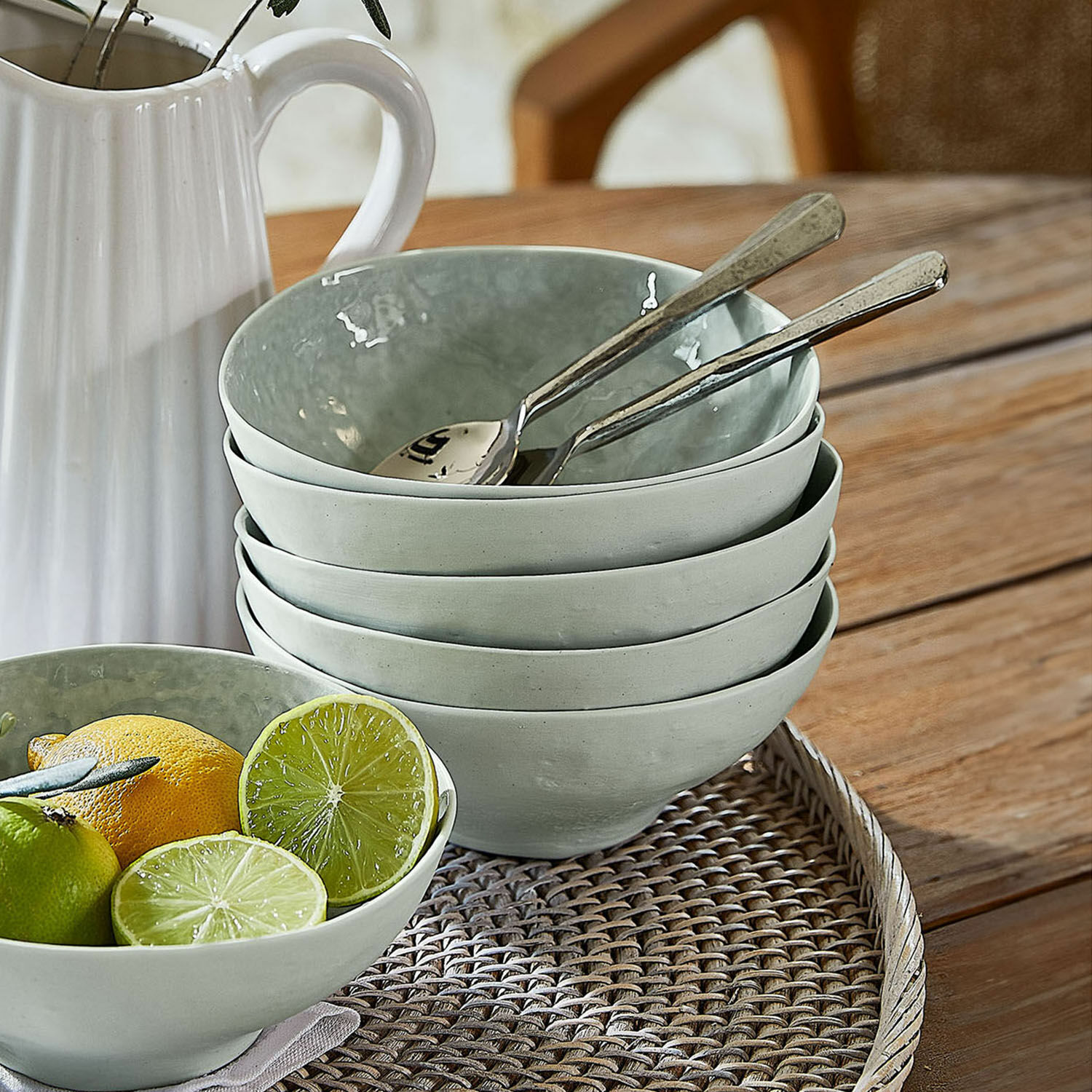 Set grauer Keramikschalen auf geflochtenem Tablett mit Früchten und Löffeln
