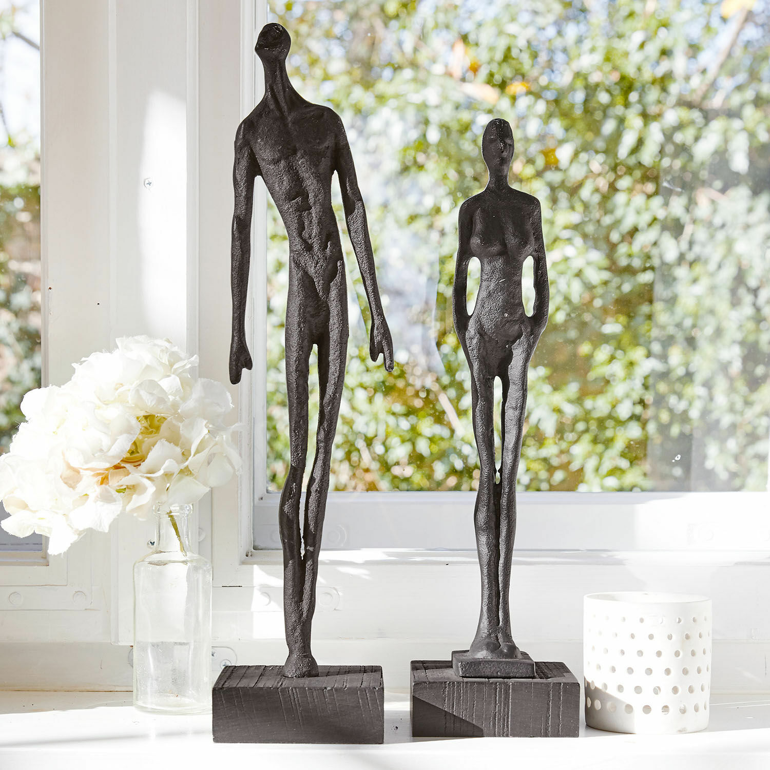 Figur 2er Set Perce Zwei schwarze Metallfiguren auf Holzsockeln vor einem hellen Fenster mit weissen Dekorationen