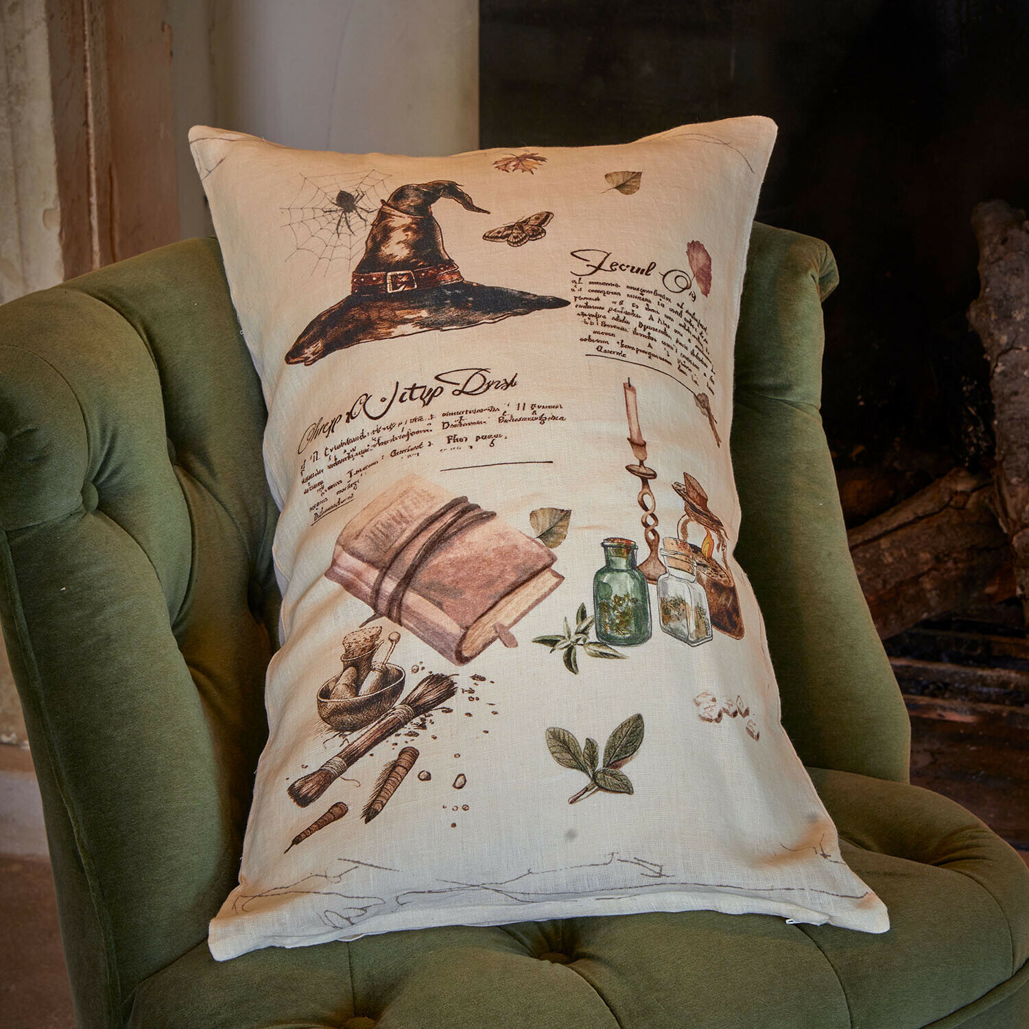 Kissenhülle Maerlinna Beiges Leinenkissen mit Aufdruck eines schwarzen Huts, Buch und Kräutern auf grünem Sessel
