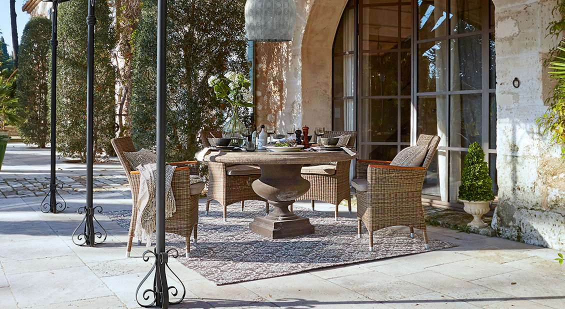 Braunes Rattan-Gartenmöbel-Set mit Polstern und Steintisch auf sonniger Terrasse