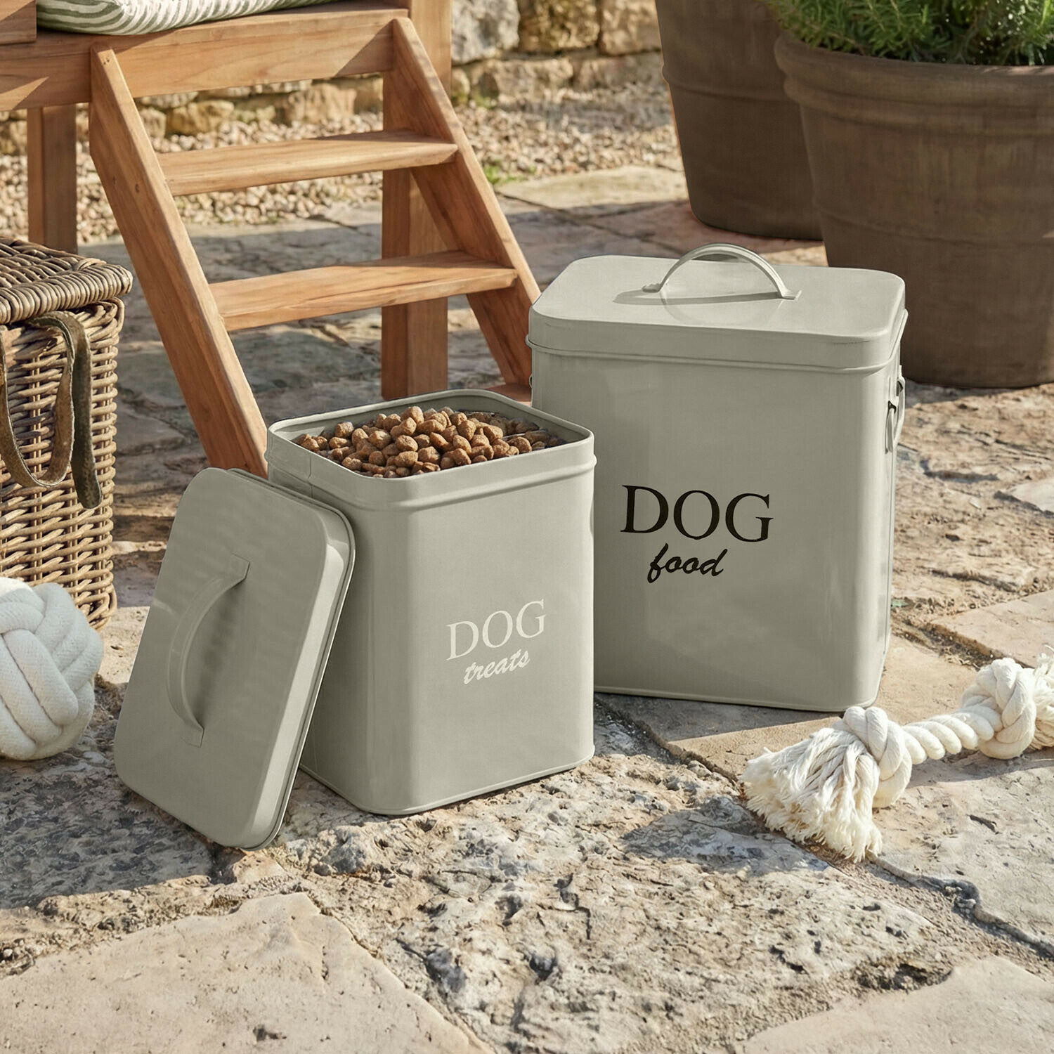 Graue Metallbehälter für Hundefutter und Leckerlis auf Steinboden im Garten