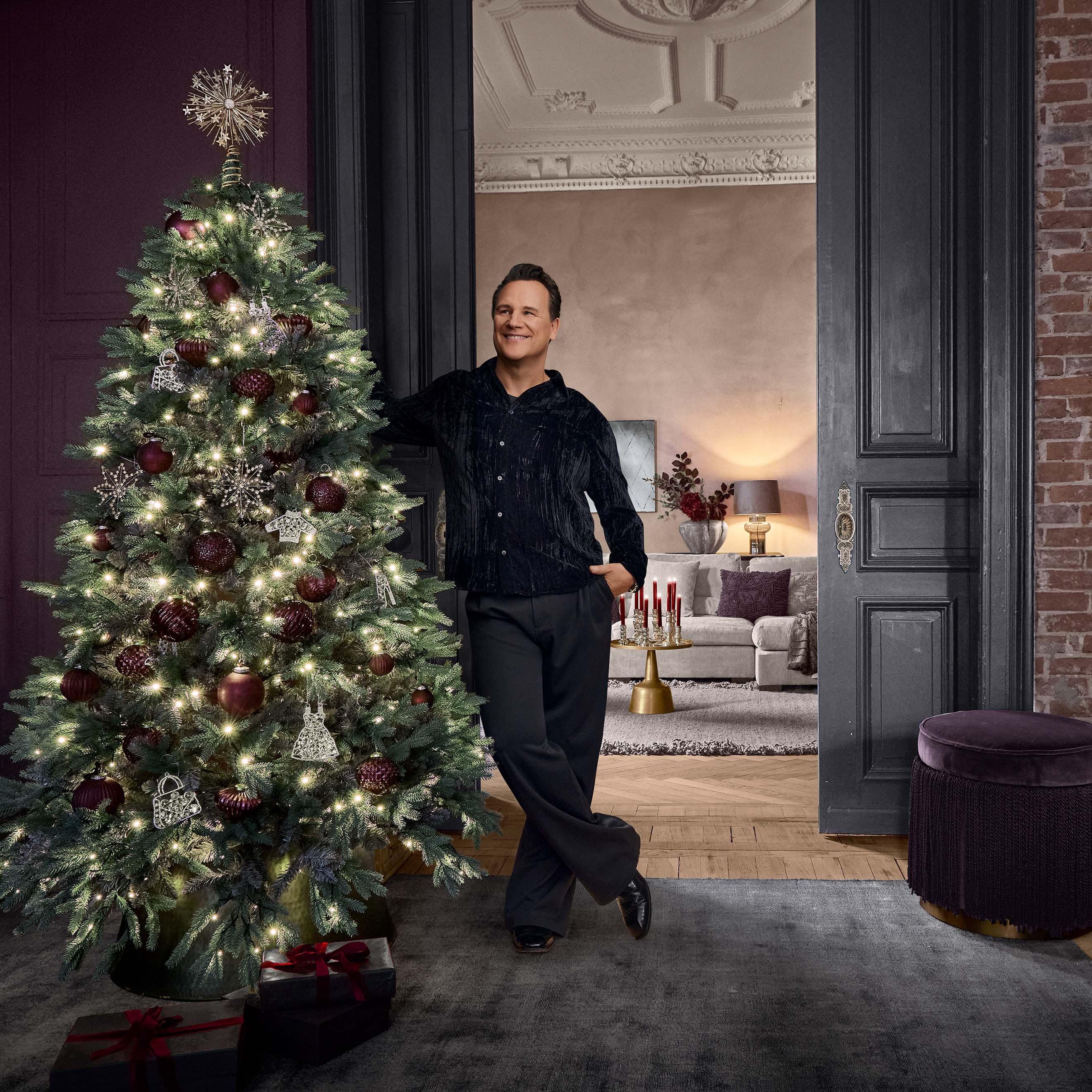 Weihnachtsbaum mit roten und silbernen Kugeln und Lichterketten in elegantem Zimmer mit Mann.