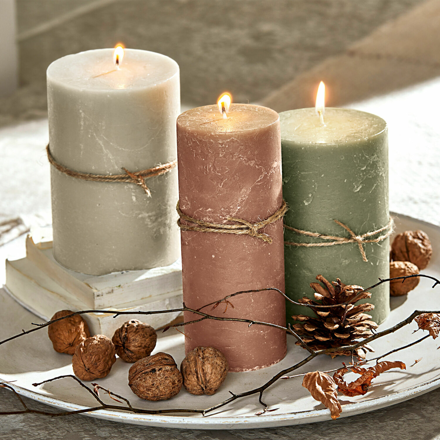 Kerze 3er Set Salis Drei brennende Wachskerzen in Beige, Rosa und Grün auf einem dekorativen Tablett mit Nüssen und Zweigen