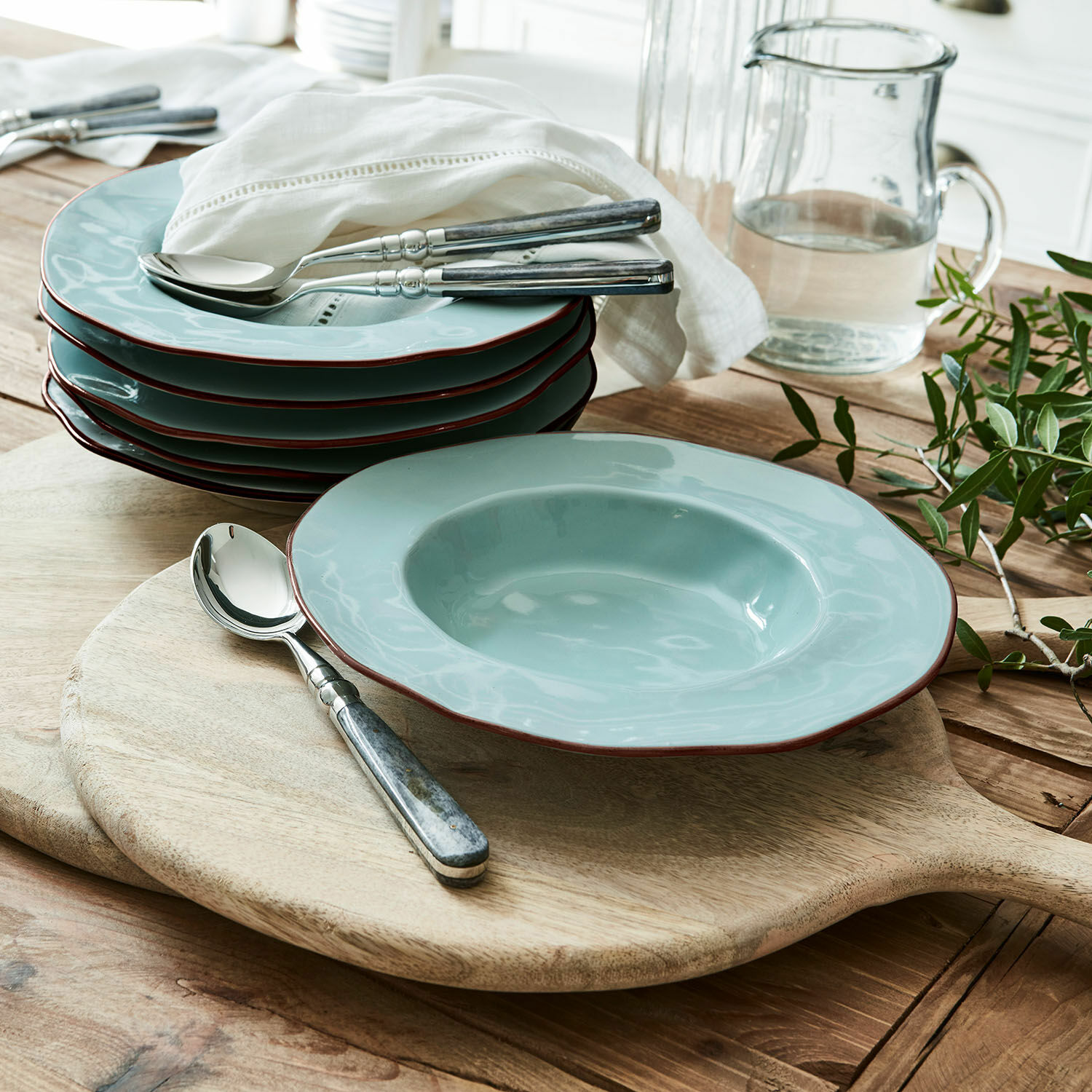 Set aus hellblauen Keramiktellern mit braunem Rand auf einem Holzbrett zum Servieren