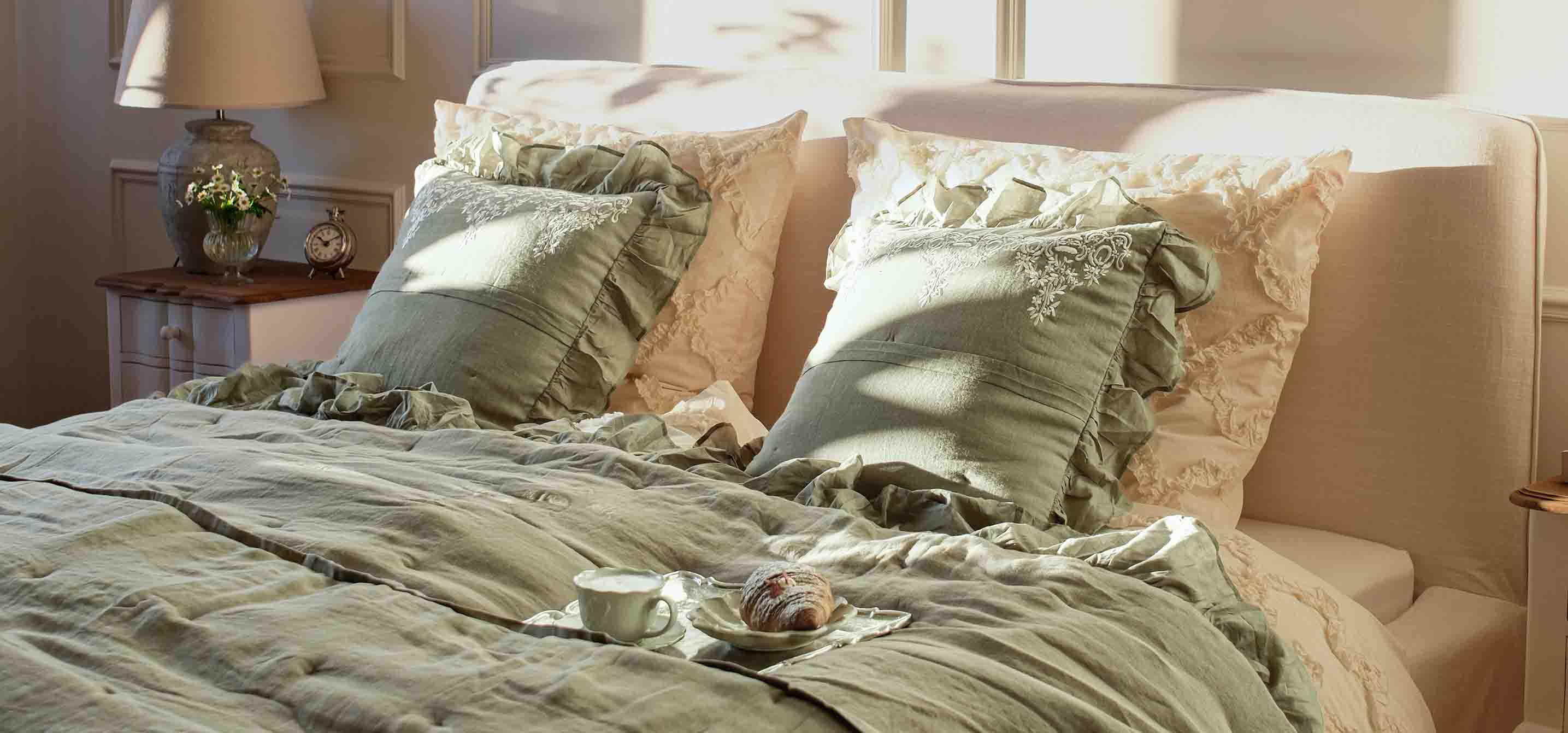 Grüne Bettwäsche und Kissen mit Rüschen auf Bett in hellem Schlafzimmer mit Lampe und Uhr