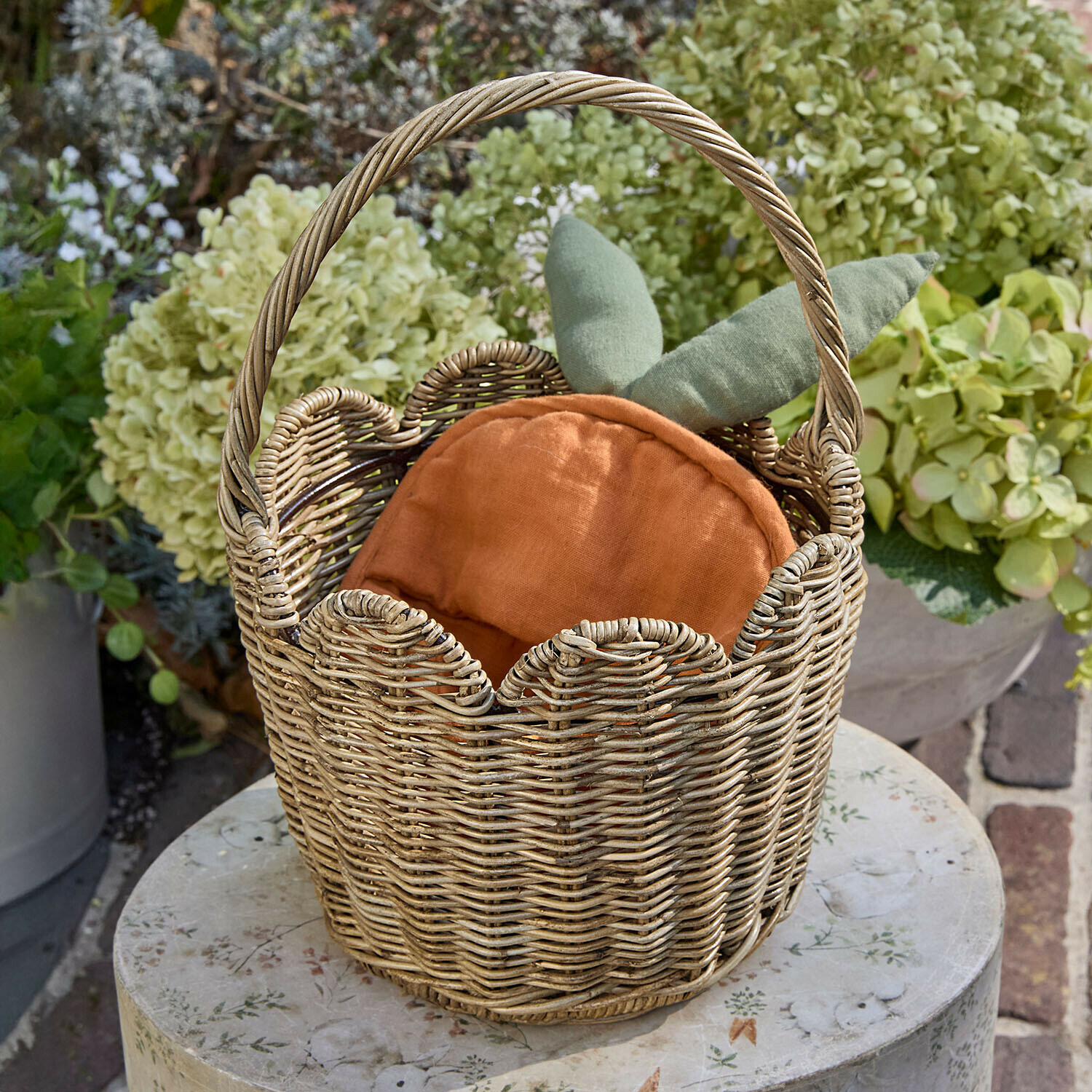 Korb Whimsywood Weidenkorb mit orangefarbenem Kissen und grünen Blättern, Gartendekoration auf rundem Tisch