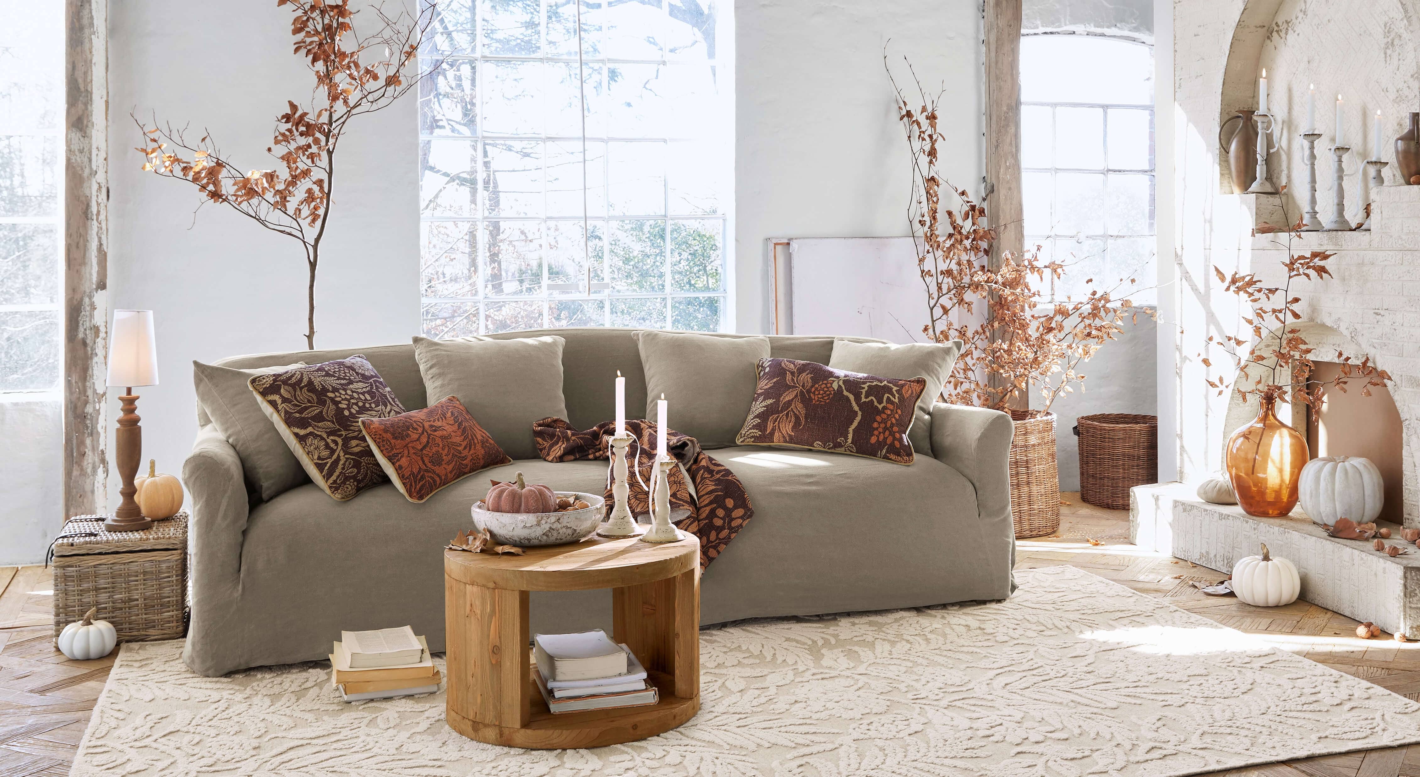 Beiges Stoffsofa in gemütlichem Wohnzimmer mit herbstlicher Dekoration und rundem Holztisch