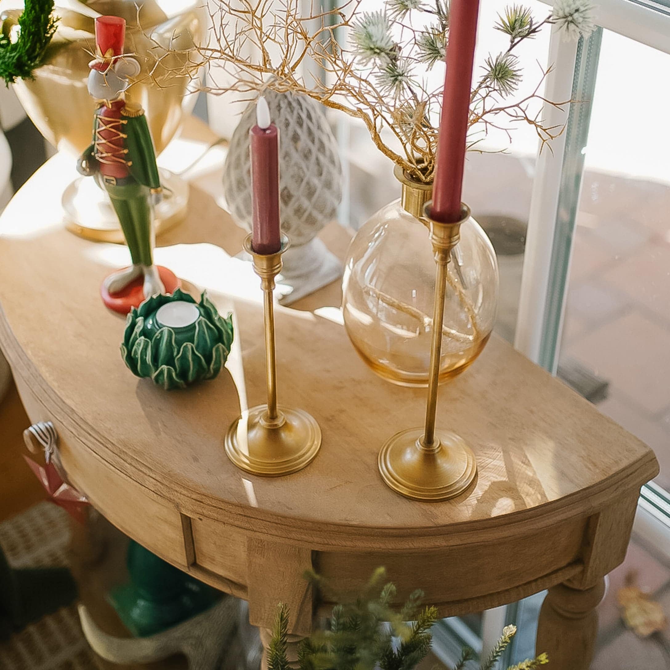 Holztisch mit Messingkerzenhaltern und weihnachtlicher Dekoration im warmen Licht.