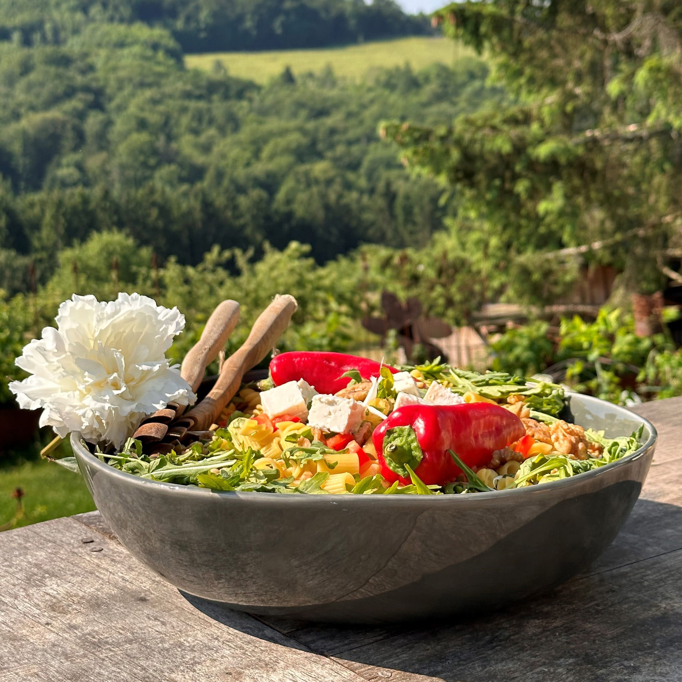 Grosse Keramikschüssel mit Salat, roter Peperoni, Feta und Rucola auf Holztisch im Freien