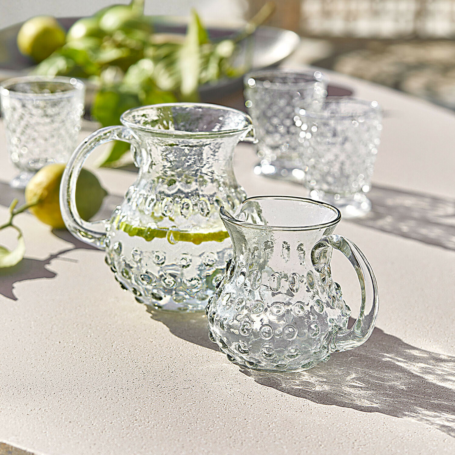 Glaskrug und kleiner Krug mit erhabener Struktur auf hellem Tisch, ideal für Sommergetränke