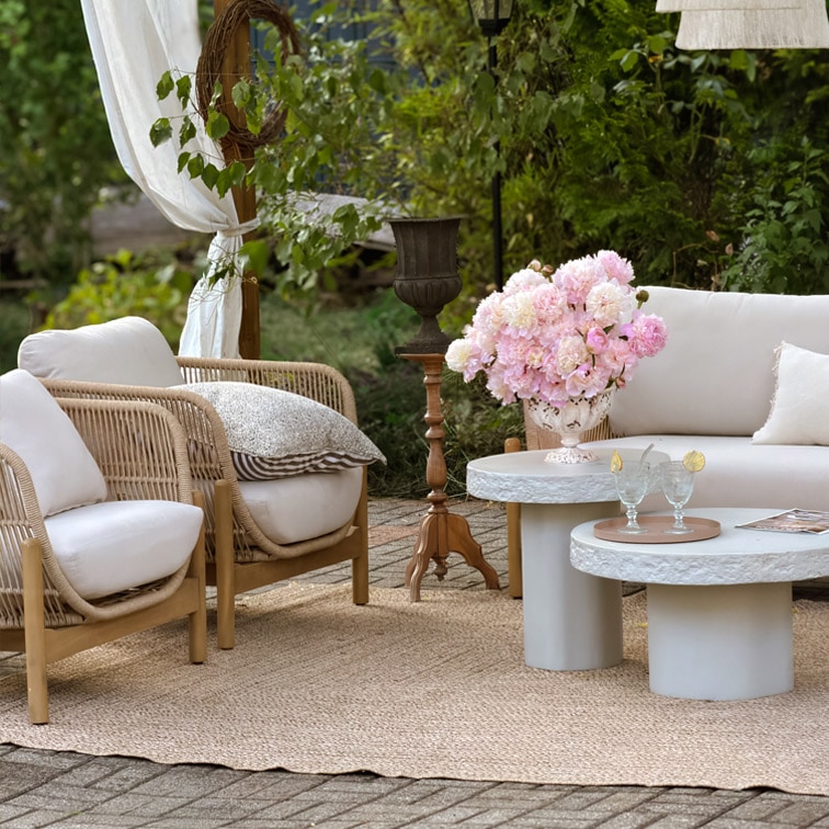 Gartenmöbel-Set mit hellen Kissen, Rattansesseln und Betontischen auf Juteteppich im Aussenbereich