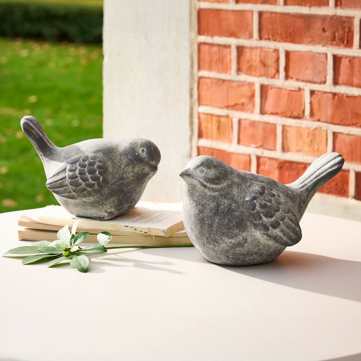 Deko-Vogel 2er Set Haldoríe Zwei graue Vogel-Figuren aus Stein auf weissem Tisch mit Buch und grünem Blatt als Dekoration